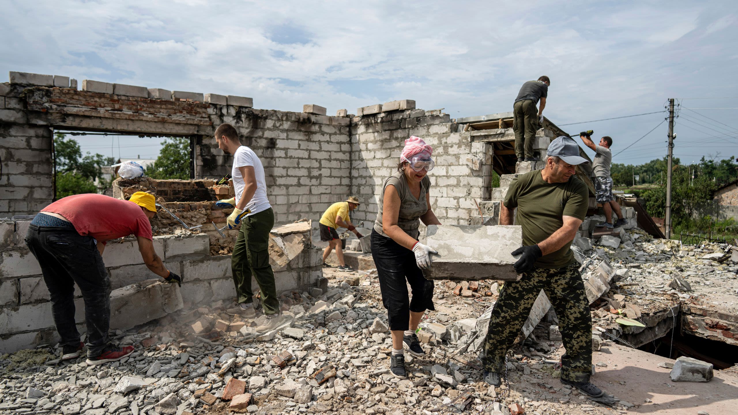 A group of men and women clear away stones from a destroyed building.
