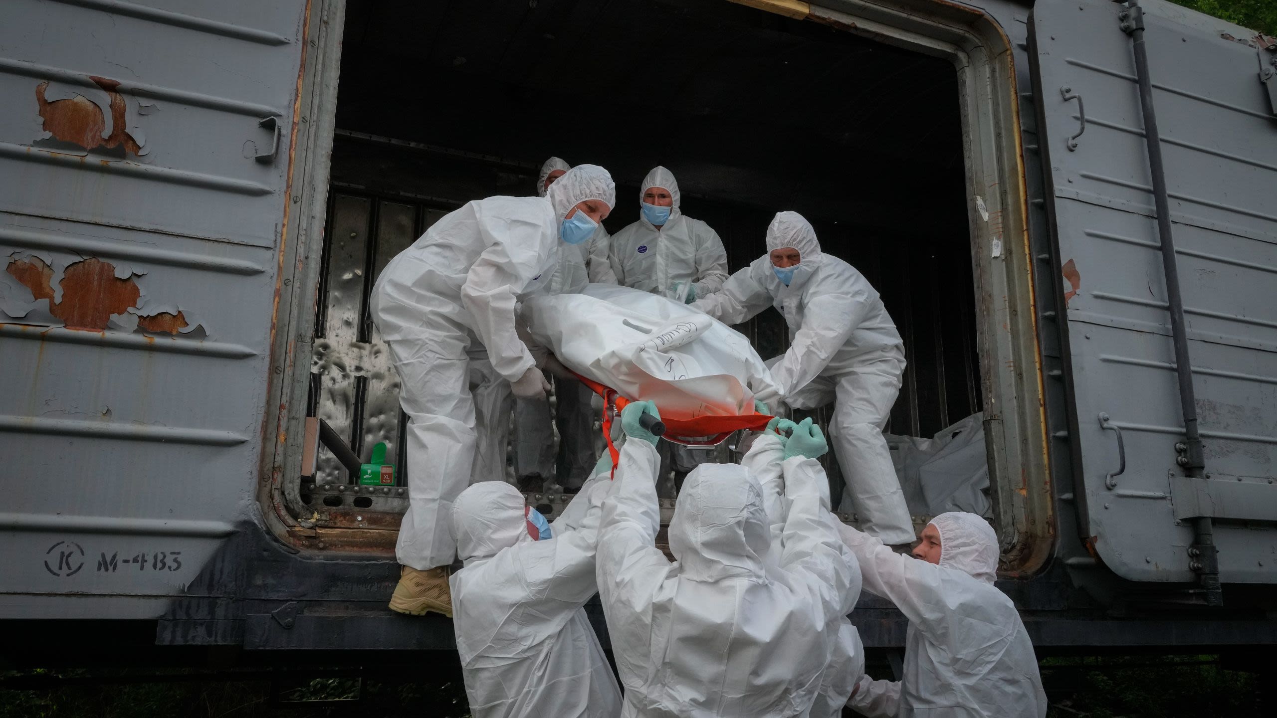 People dressed in white hazmat suits lift a body bag into a train car.