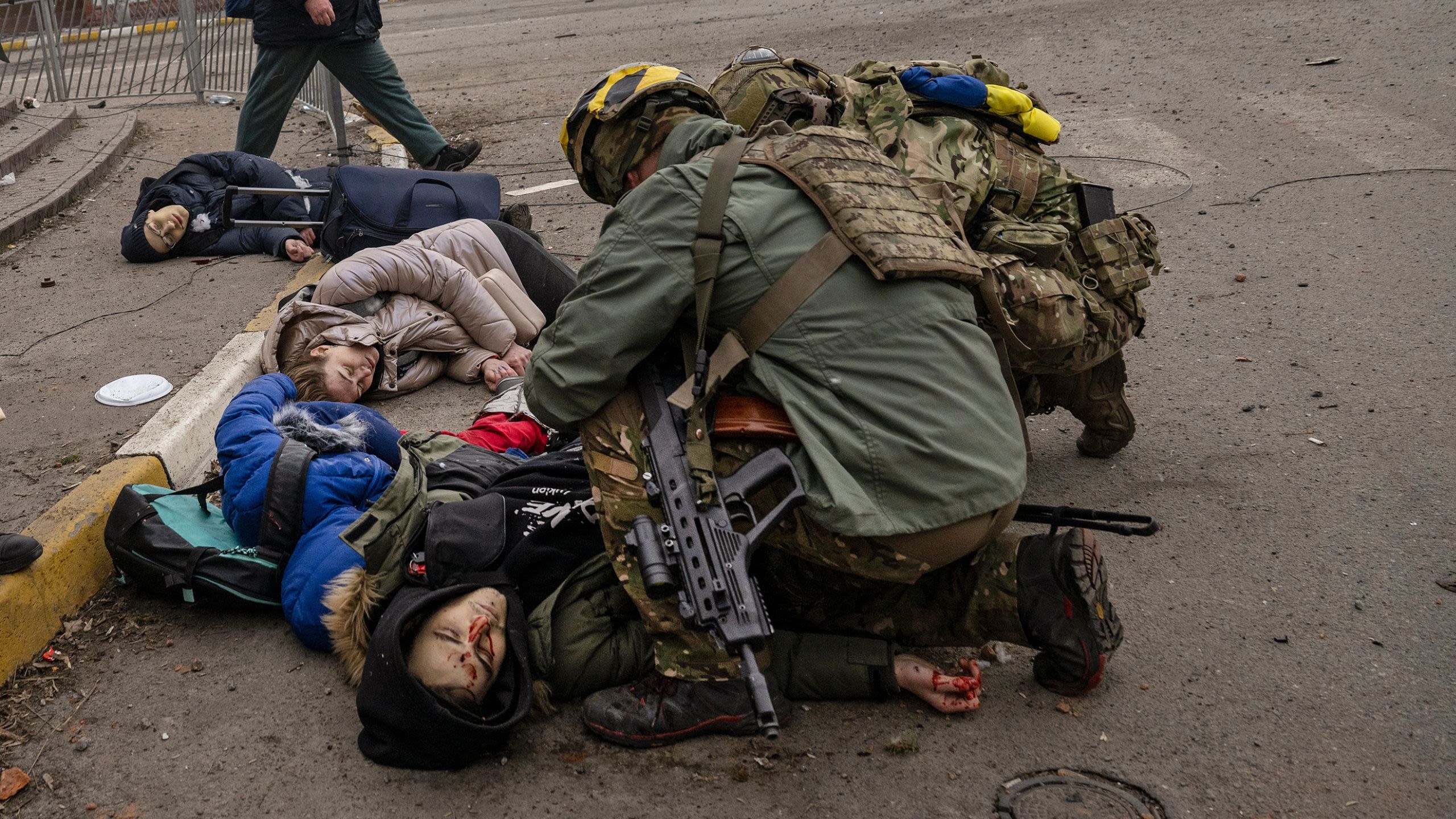 Men in military uniforms tend to the bodies of a woman and two children who lie dead in the street.