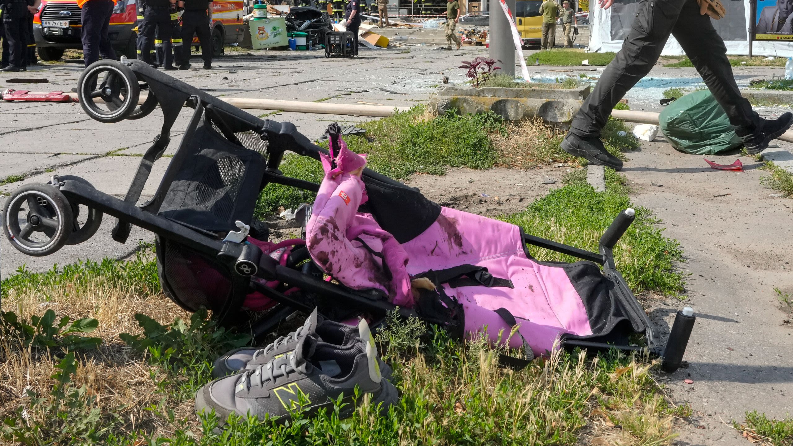 A baby stroller lies on its side next to pair of shoes in front of bombed-out building.