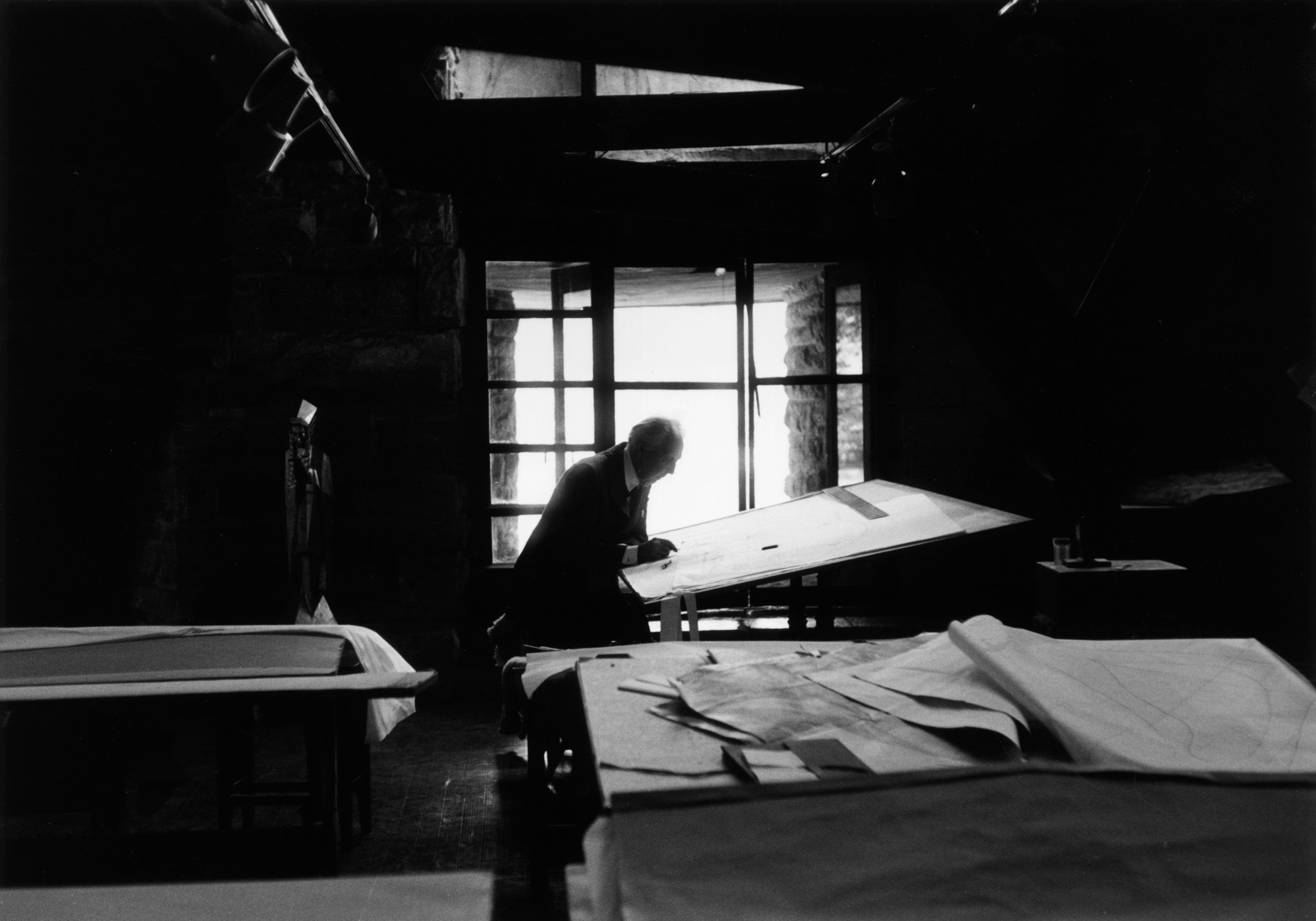 Man working at a drafting table while silhouetted against a large window (© Tony Vaccaro/Hulton Archive/Getty Images)