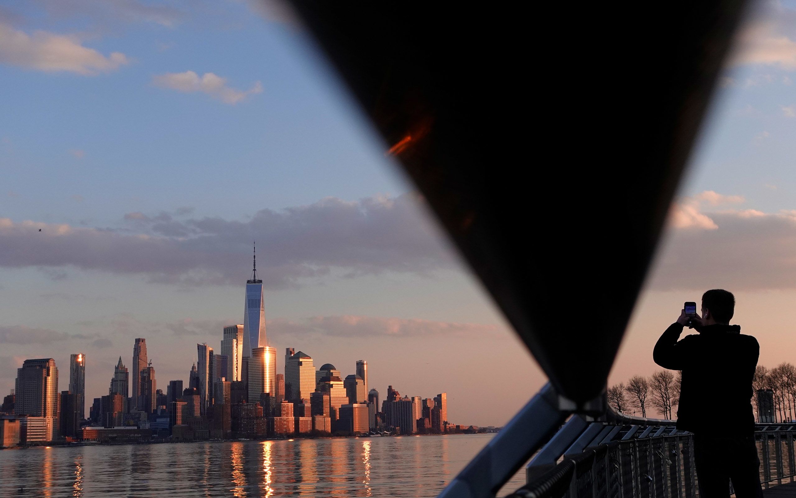 A silhouette of a person taking a picture of the New York City skyline at sunset, with One World Trade Center prominently visible among the buildings (© Gary Hershorn/Getty Images)