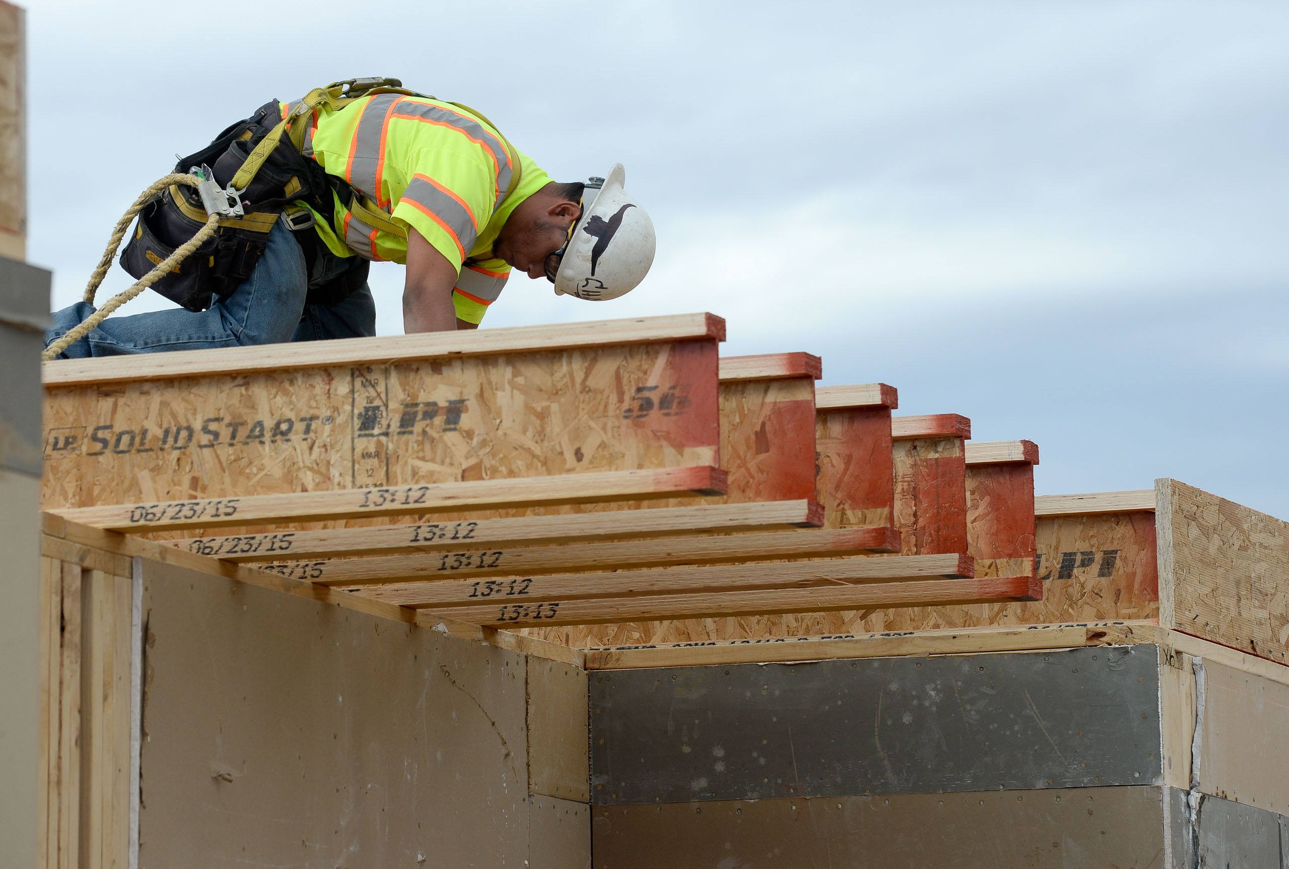 A construction worker in a safety harness is leaning over the edge of a partly framed wooden structure (© Lewis Geyer/Digital First Media/Boulder Daily Camera/Getty Images)