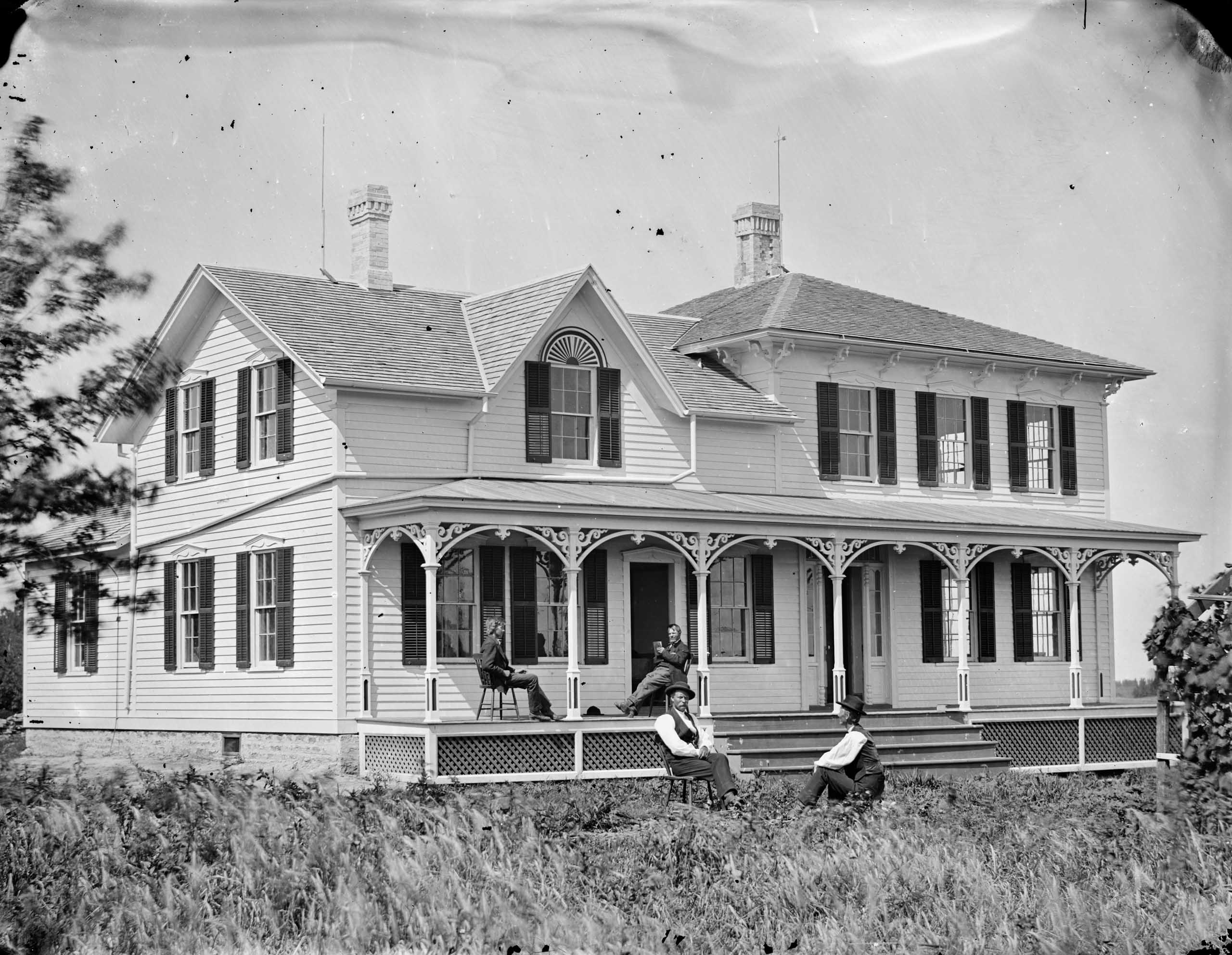 People sitting on a wraparound porch on a large, two-story wooden house (© Andreas Larsen Dahl/Wisconsin Historical Society/Getty Images)