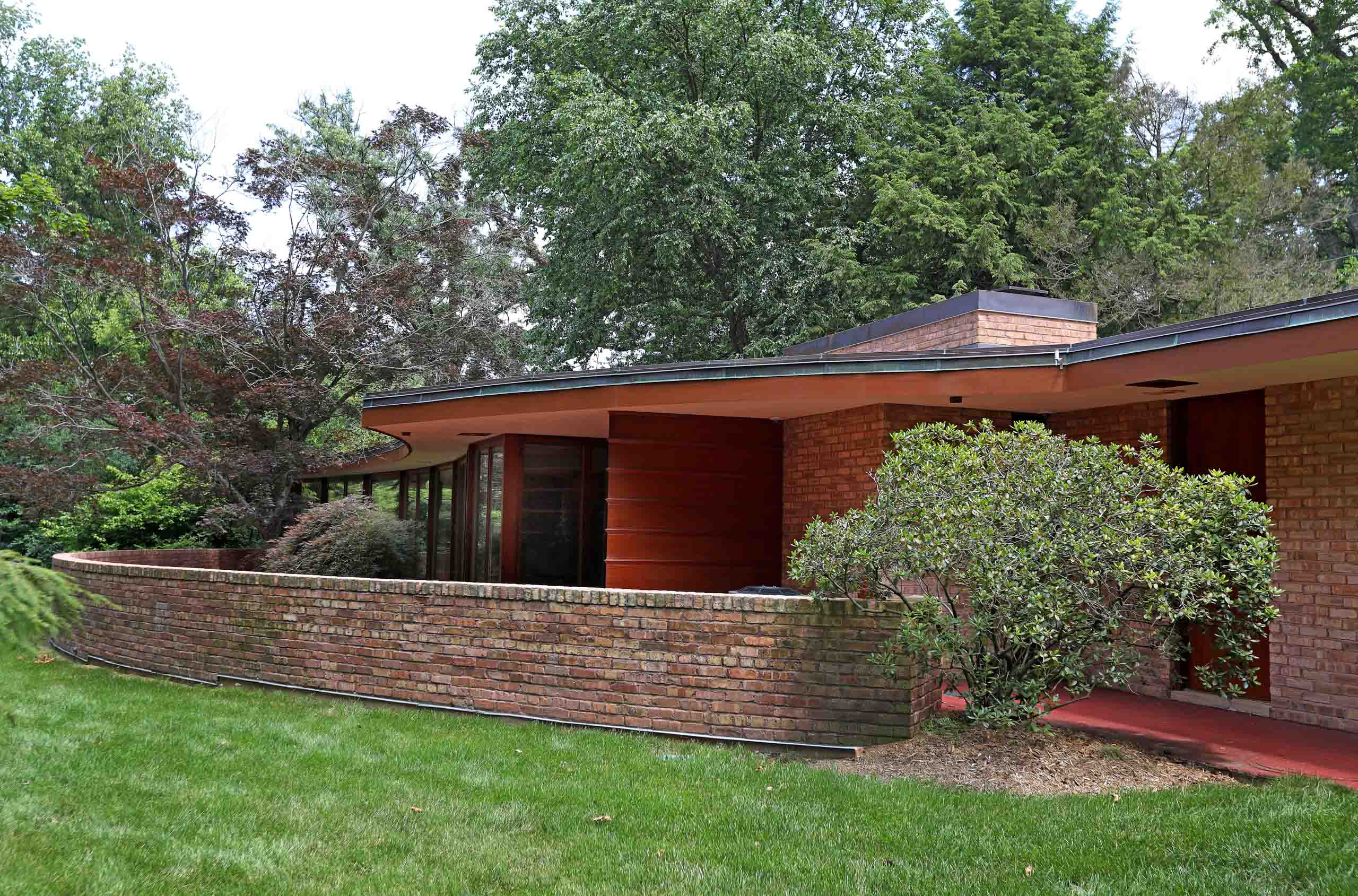 A photo shows a house with a low, flat roof with deep eaves and a curved brick wall in the foreground (© Raymond Boyd/Getty Images)