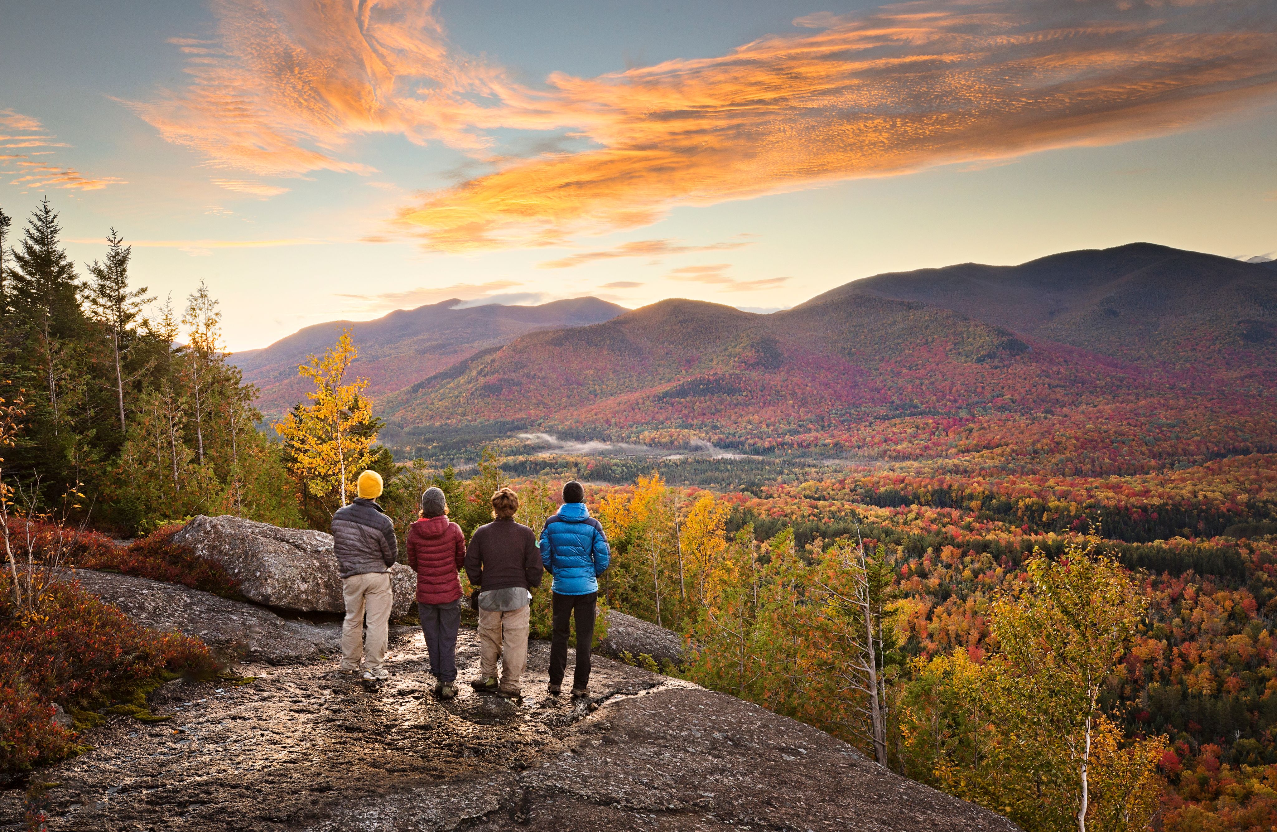 Four hikers standing on a rocky overlook, watching fall foliage spread across mountain ridges (Patricia Thomas/Shutterstock.com)