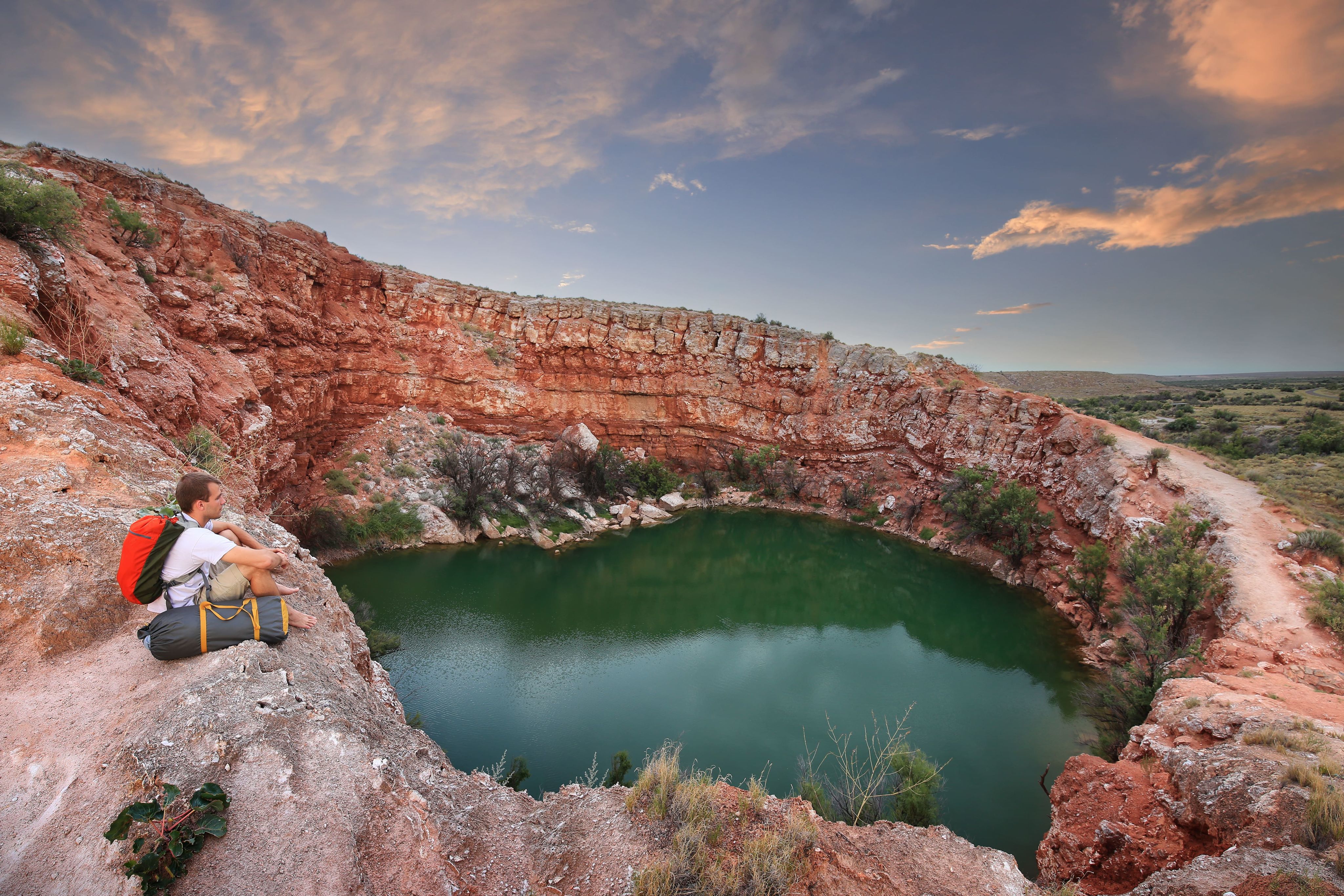 Backpacker sitting on rocky cliff overlooking pool inside canyon at sunset (© Megan Betteridge/Shutterstock.com)