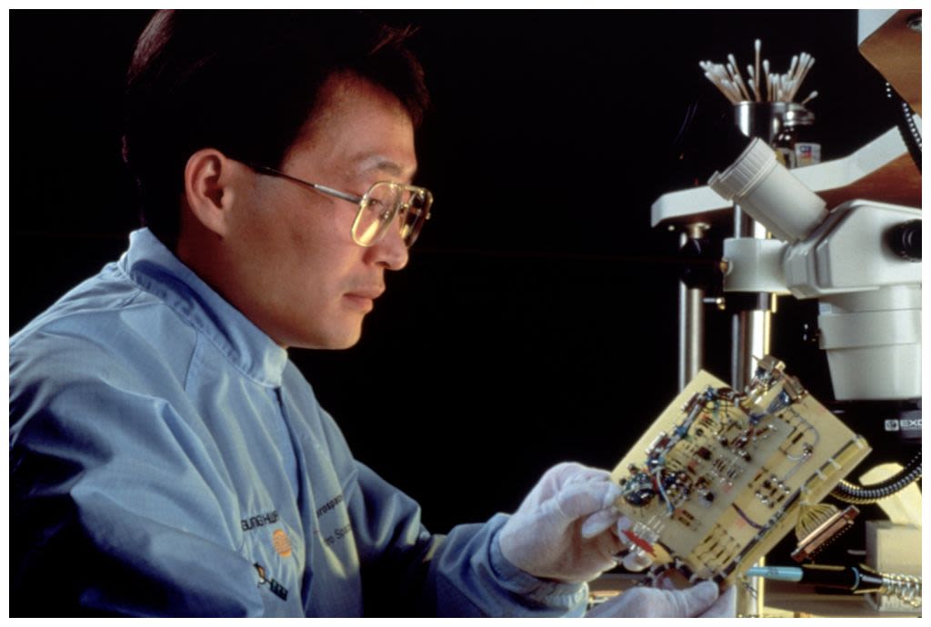 Gloved technician assembling a green circuit board (© Brownie Harris/Getty Images)