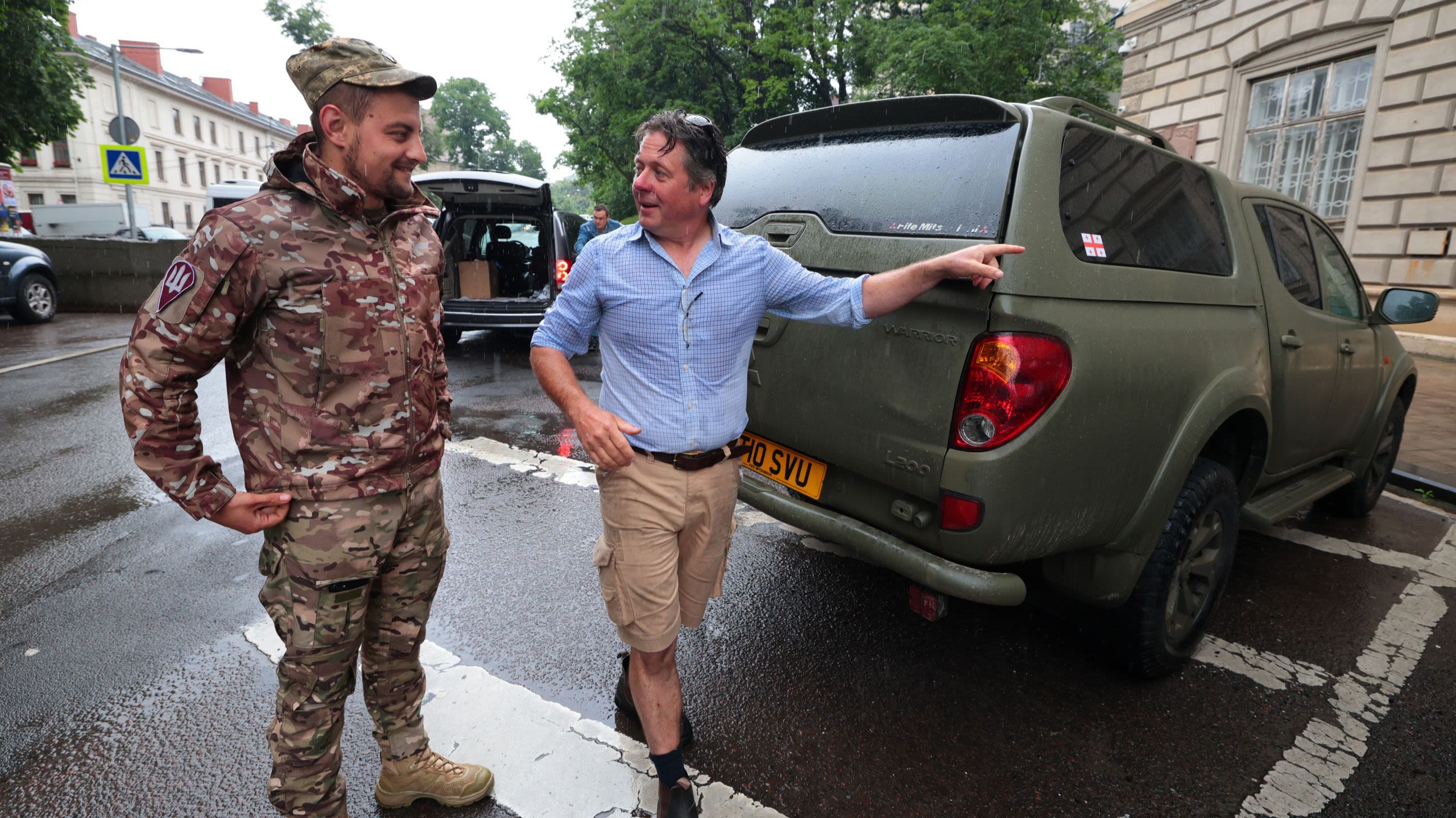 Man gesturing while talking and walking with man in military uniform at rear of pickup truck (© Alona Nikolaievych/Ukrinform/NurPhoto/Getty Images)
