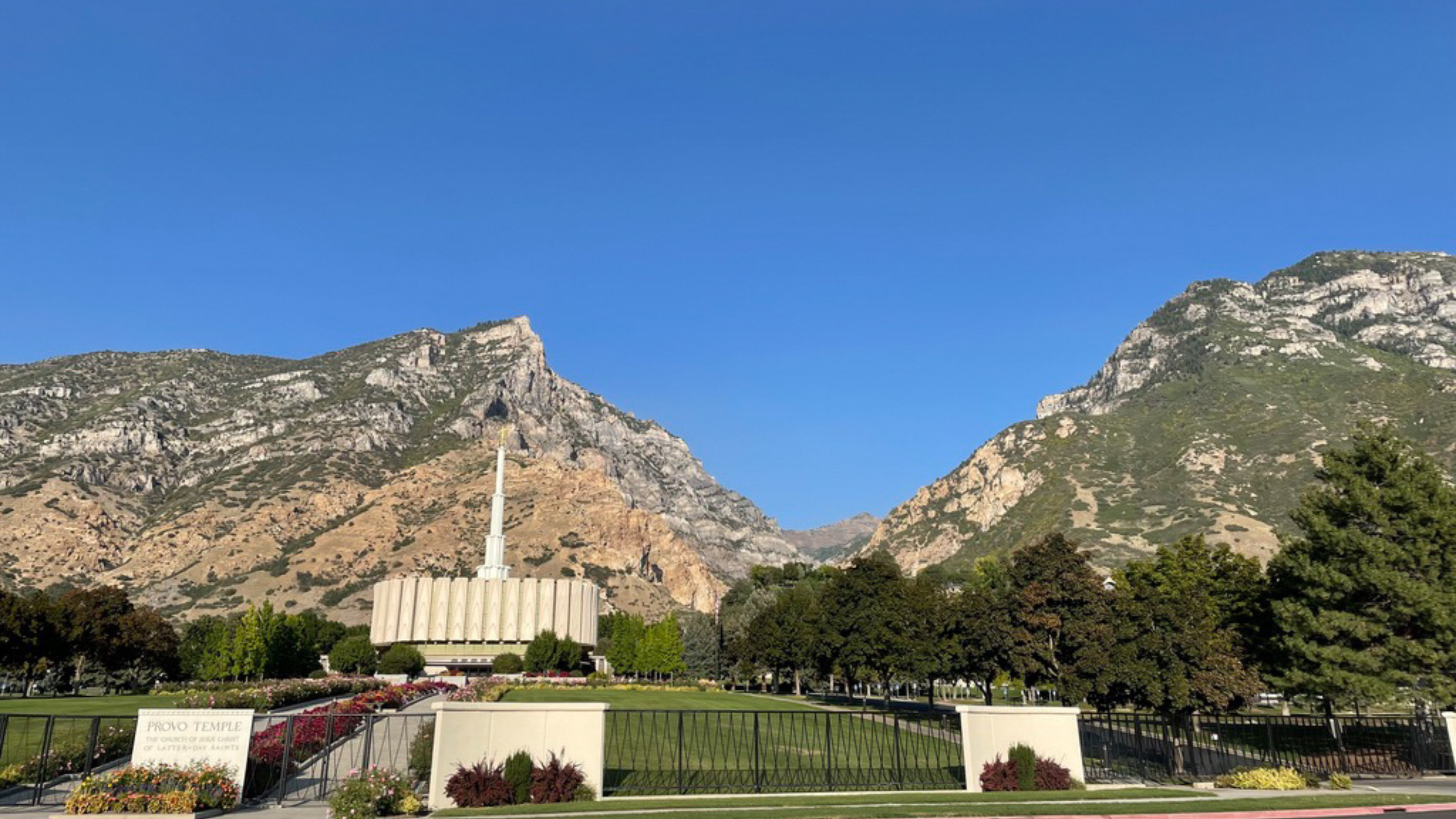 a round building with a a larger spire sits on a rolling green lawn with mountains in the background