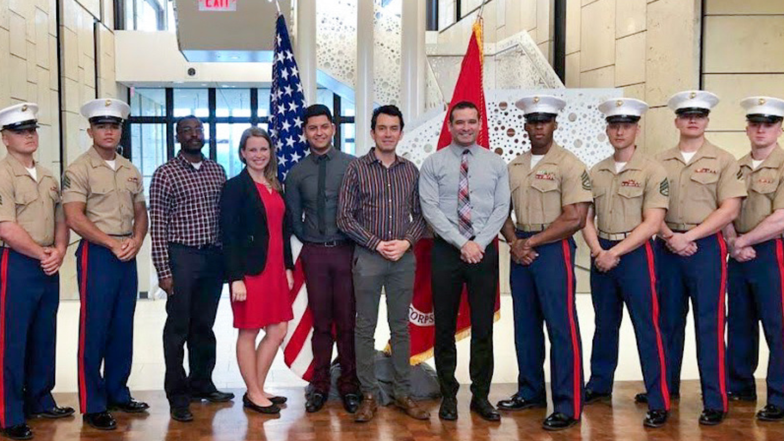 a large group of adults stand at attention in front of a U.S. flag