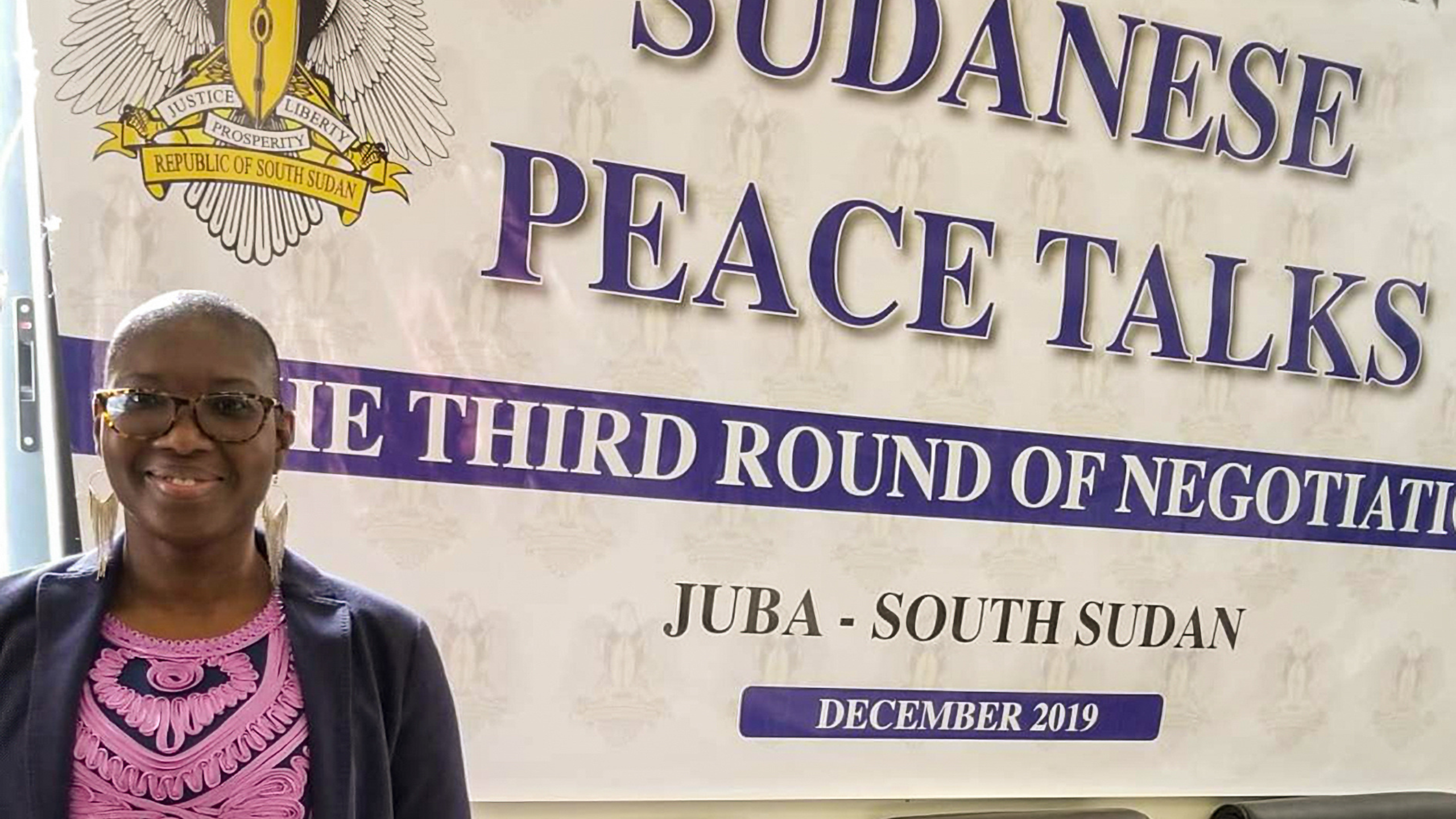 a woman stands in front of a sign that reads "Sudanese Peace Talks"