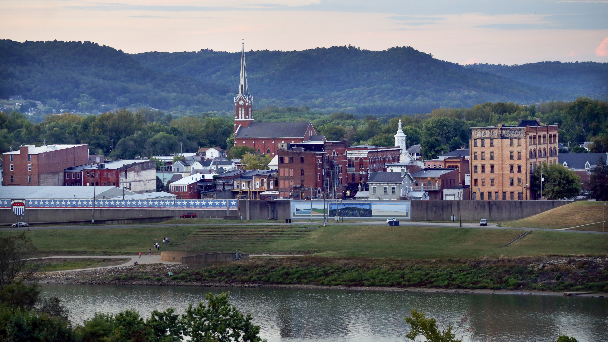 A small city sits along the edge of a river with mountains in the background
