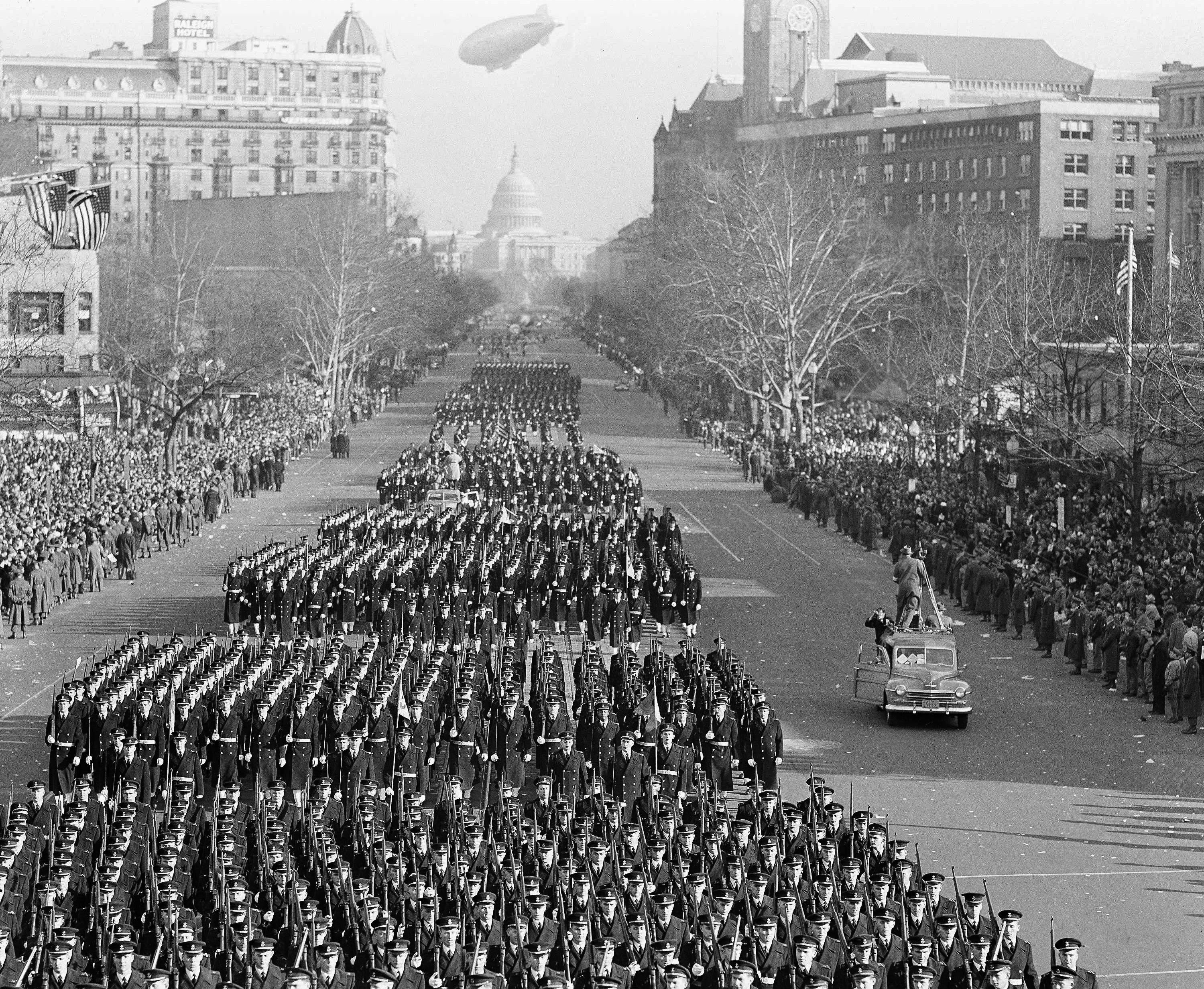 Black-and-white image of an inaugural parade with military formations marching on Pennsylvania Avenue, the U.S. Capitol visible in the distance (© AP)