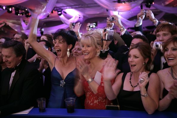 A group of formally dressed attendees cheering and waving at an inaugural ball (© Brooks Kraft LLC/Corbis/Getty Images)