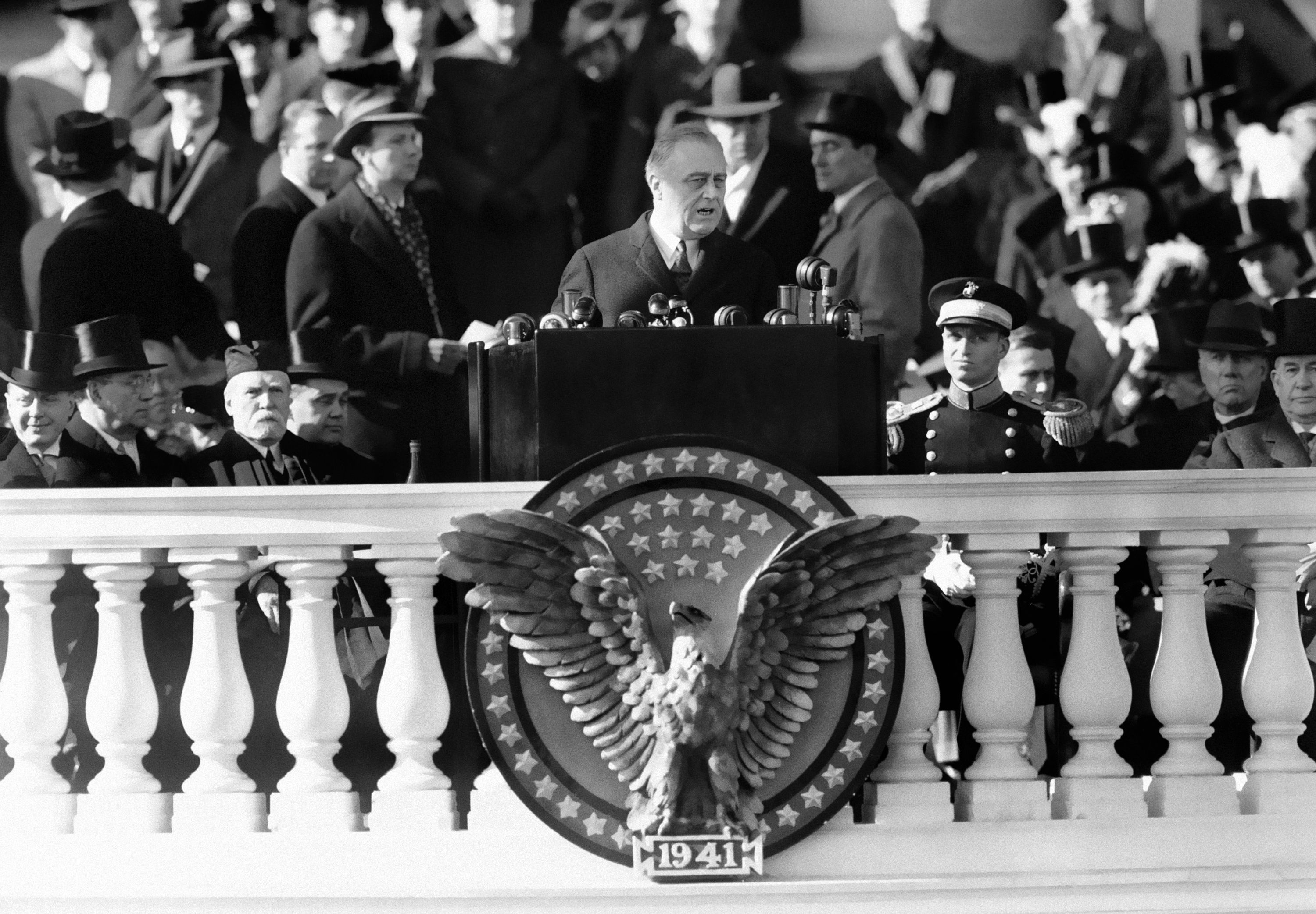 Franklin D. Roosevelt delivers his 1941 inaugural address, standing behind a lectern adorned with a large eagle and patriotic decorations (© AP)