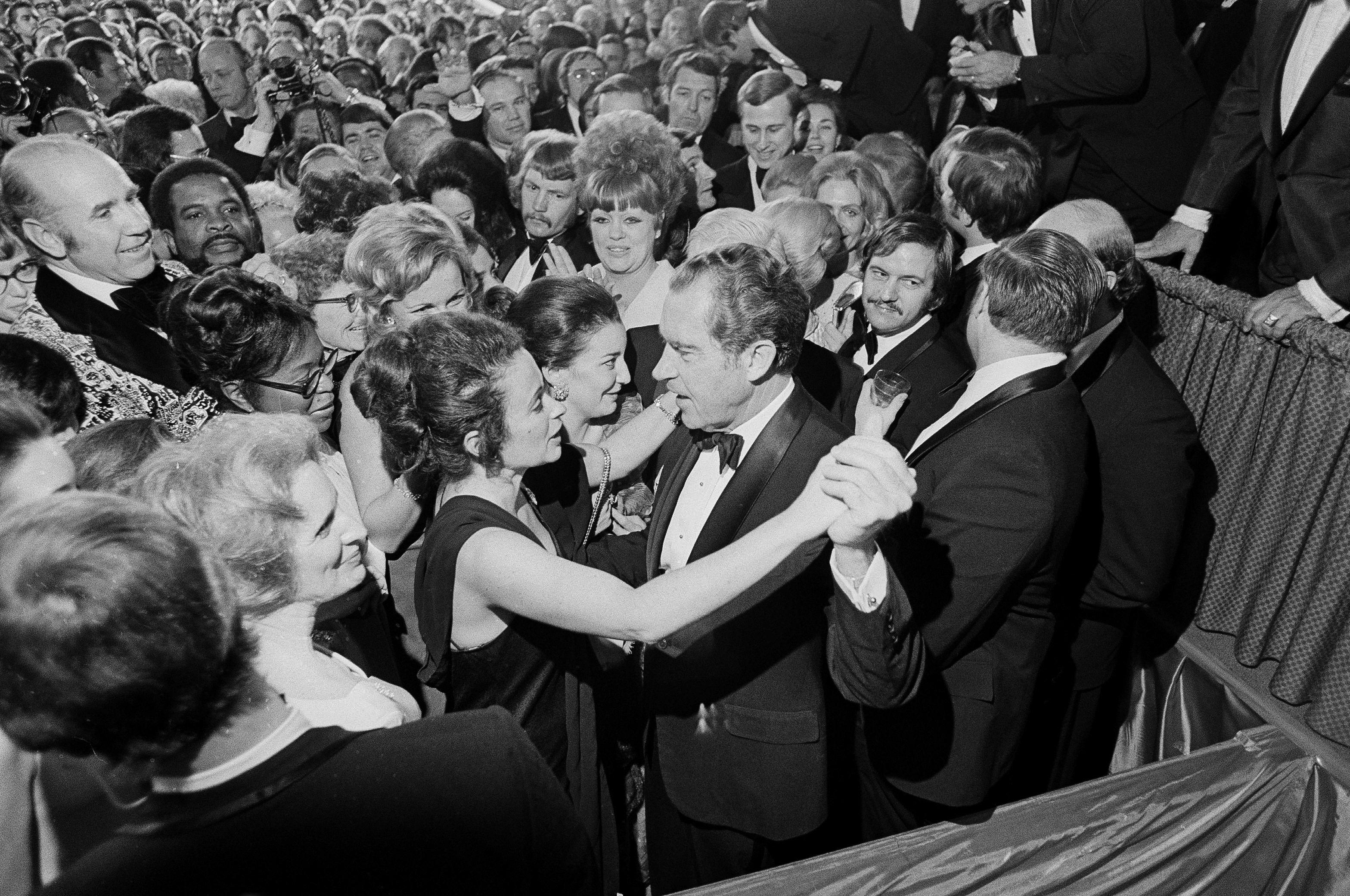 Richard Nixon dancing at an inaugural ball, surrounded by a crowd of smiling and cheering guests (© AP)