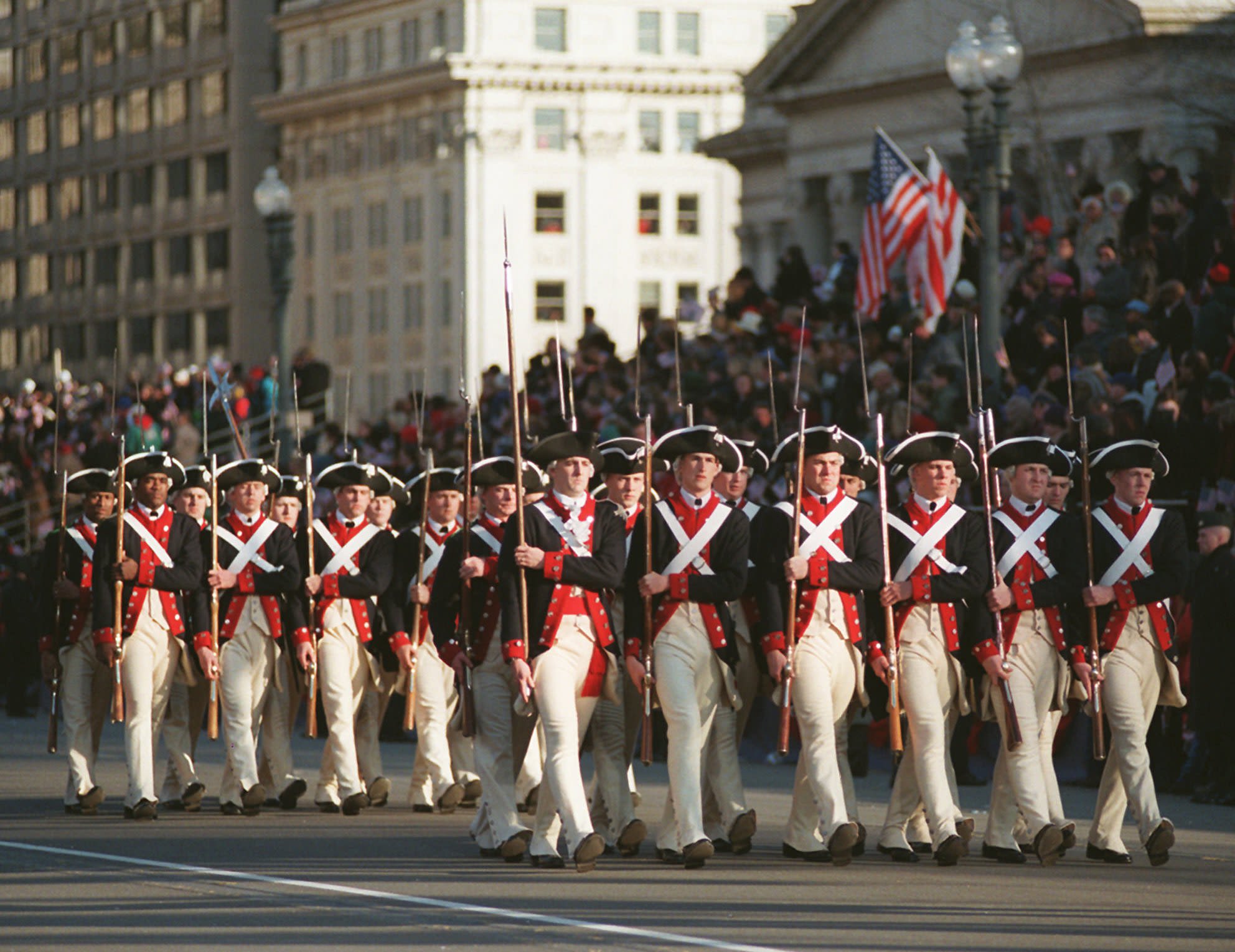Group of men dressed as colonial soldiers in red and navy uniforms marching with rifles in an inaugural parade (© Rick Bowmer/AP)