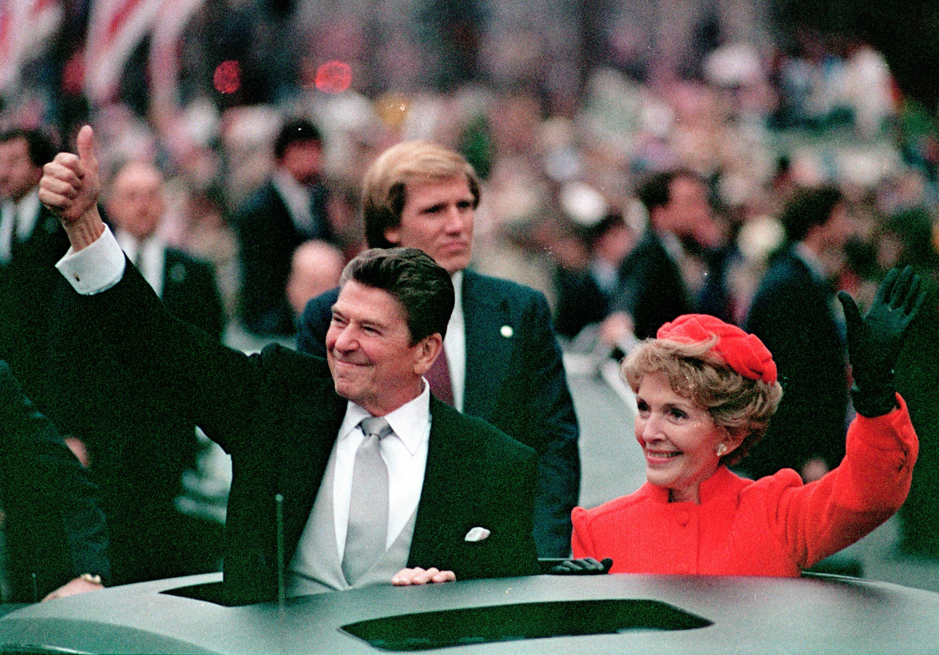Ronald Reagan and Nancy Reagan waving and smiling from an open car during the inaugural parade, with Reagan giving a thumbs-up (© AP)