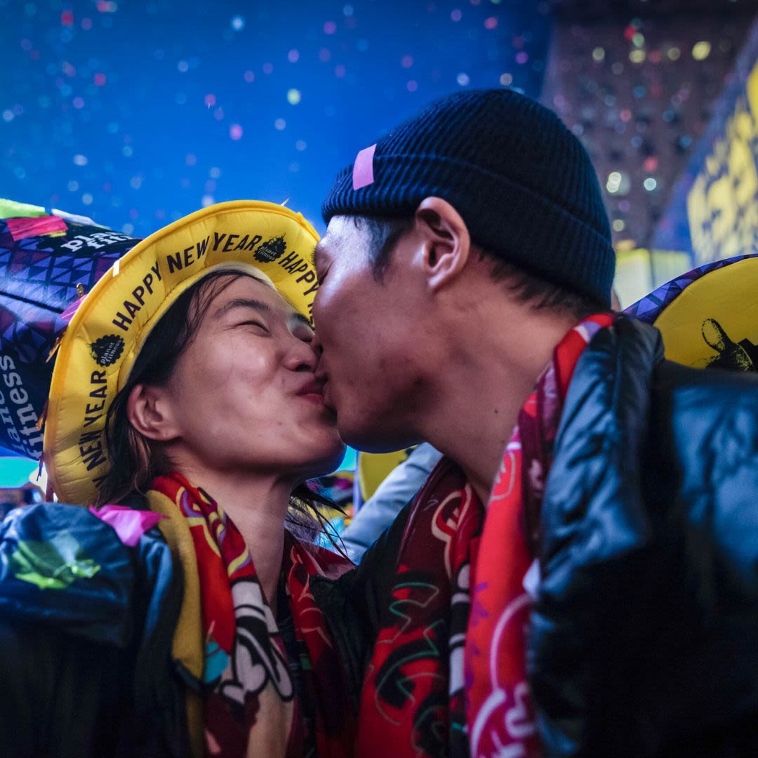A couple celebrating New Year's Eve, sharing a kiss while wearing colorful party hats that read “Happy New Year”