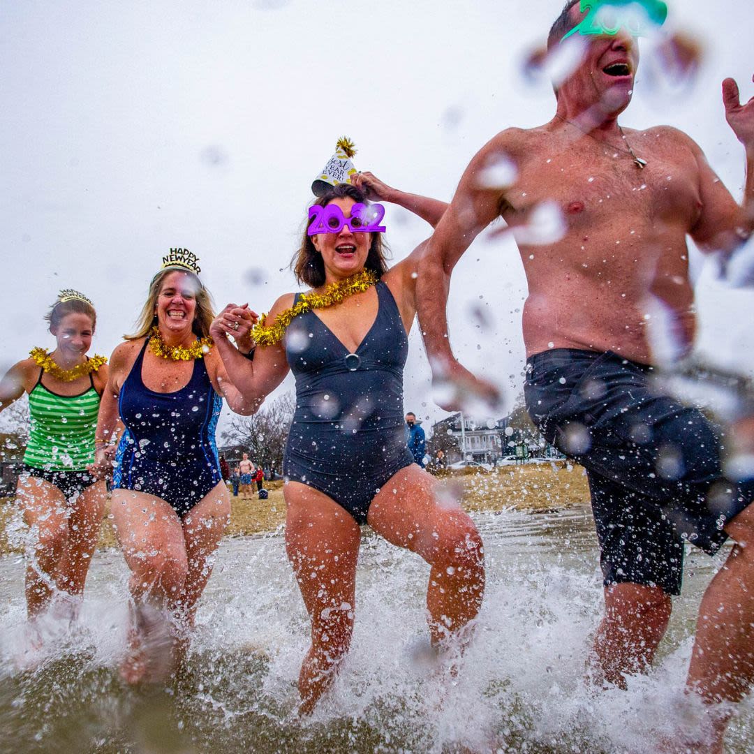 A group of people running into icy water wearing festive hats and accessories during a Polar Bear Plunge event
