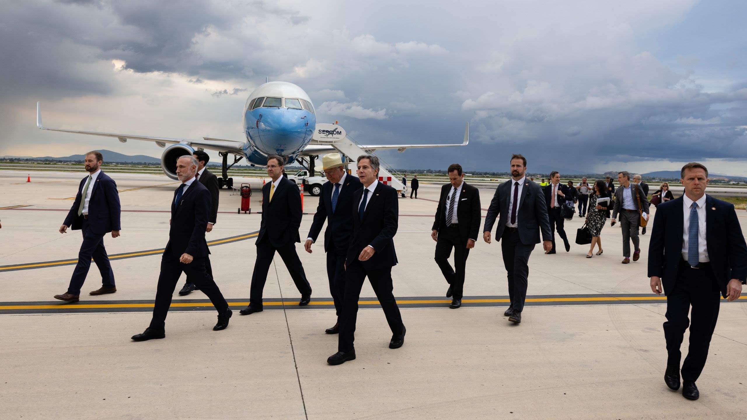 Secretary Blinken walking on tarmac surrounded by his staff and Diplomatic Security agents