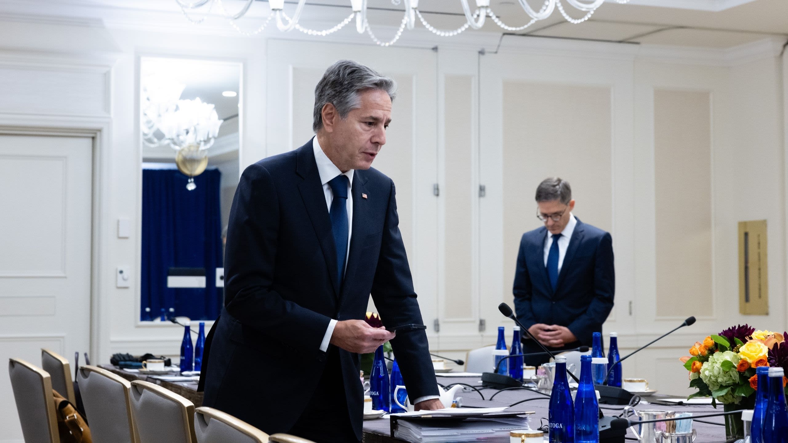 Secretary Blinken using a speaker phone at a table set up for a meeting