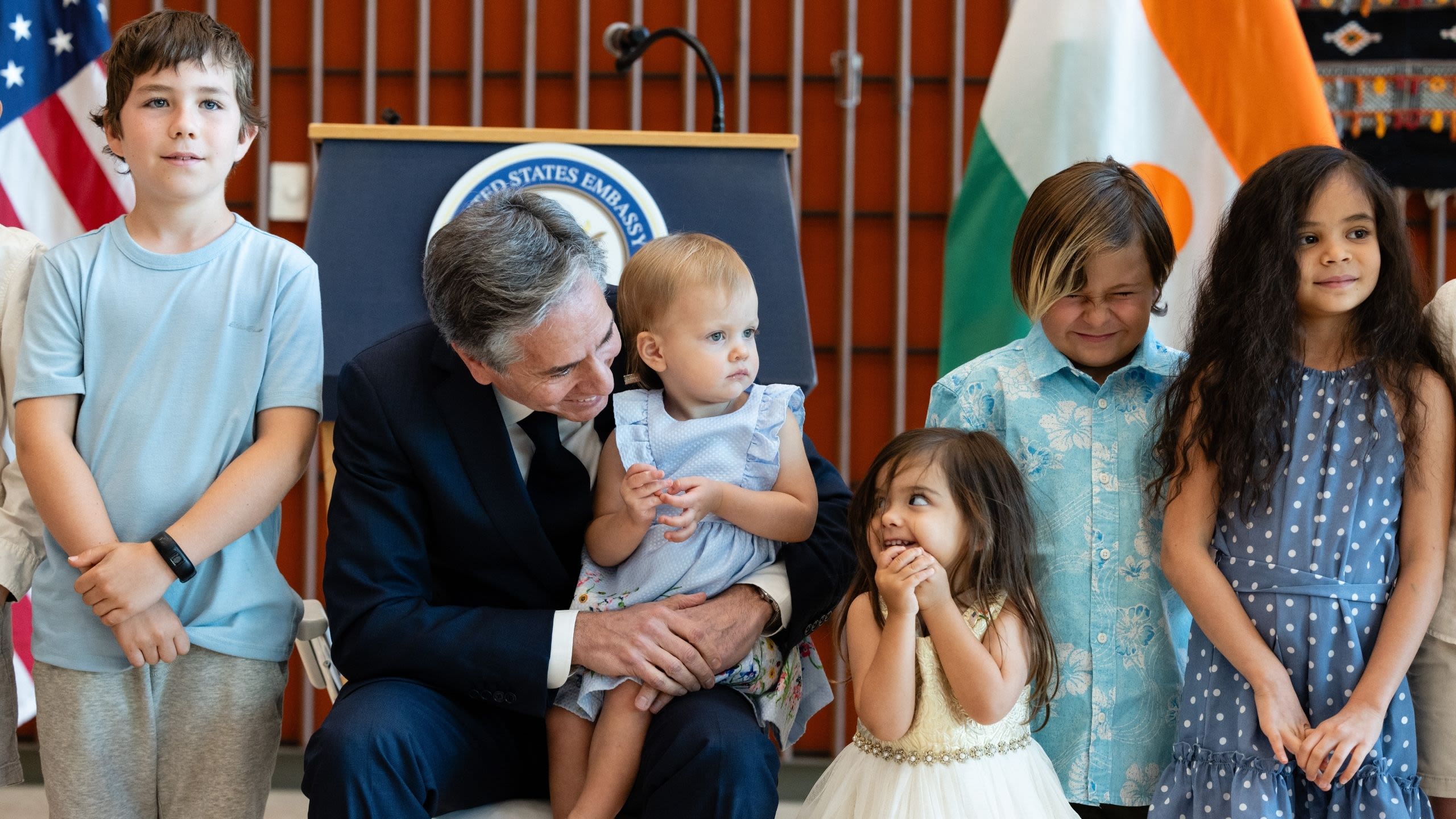 Secretary Blinken holding a child on his lap as other children stand nearby
