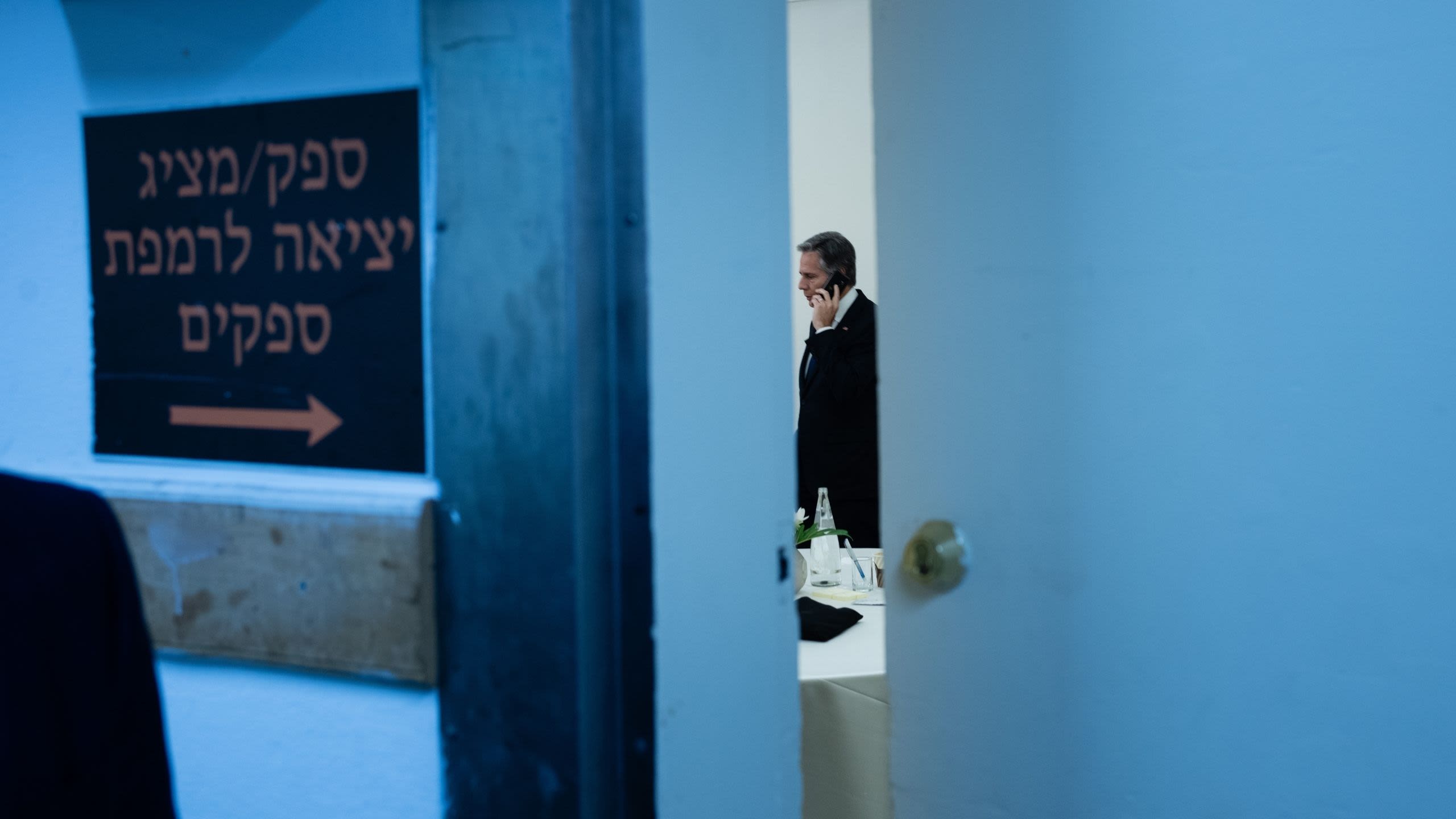 Secretary Blinken speaking on a phone as seen through a crack in an open door