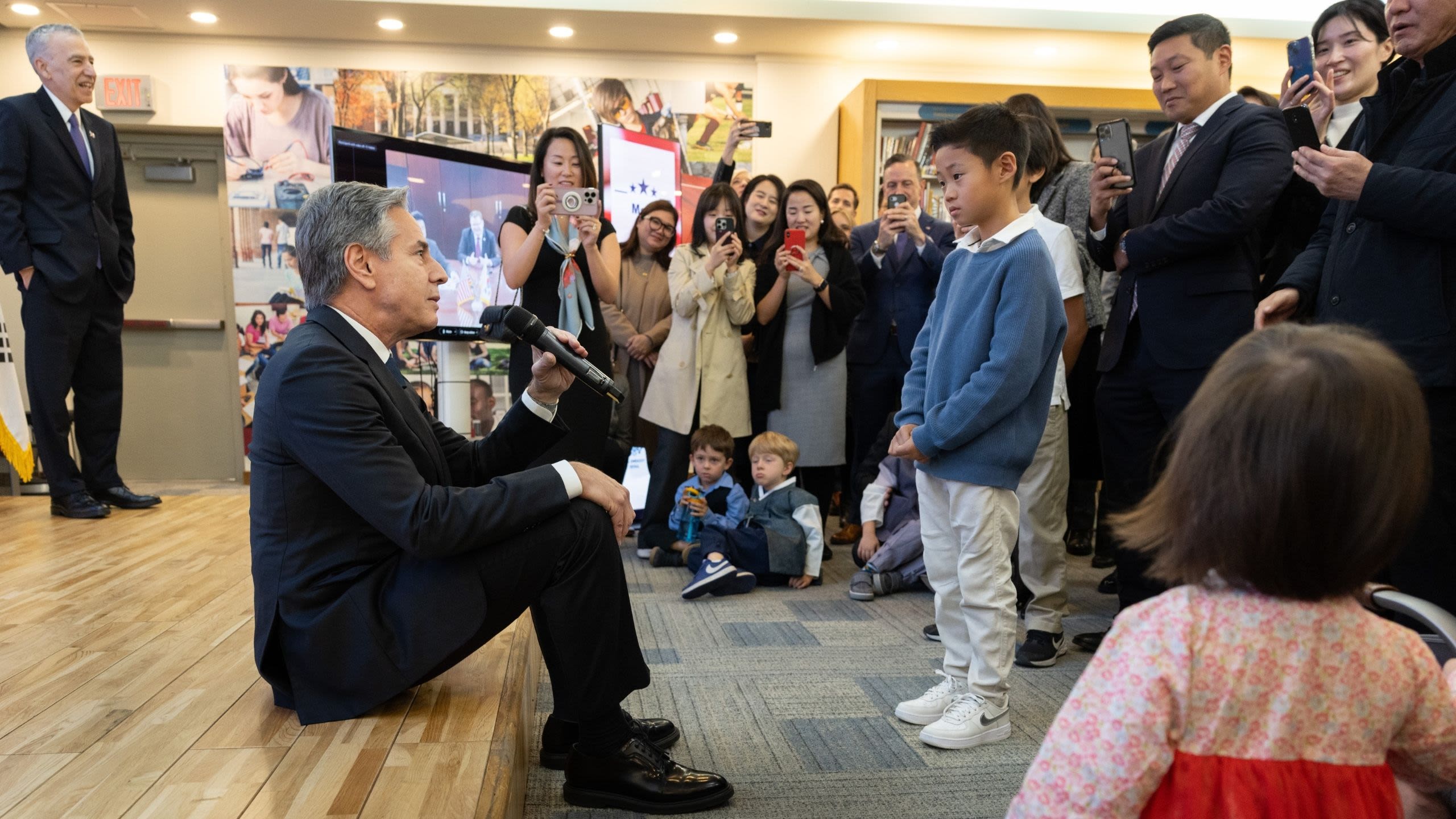 Secretary Blinken sitting on a platform while talking to a child standing before him