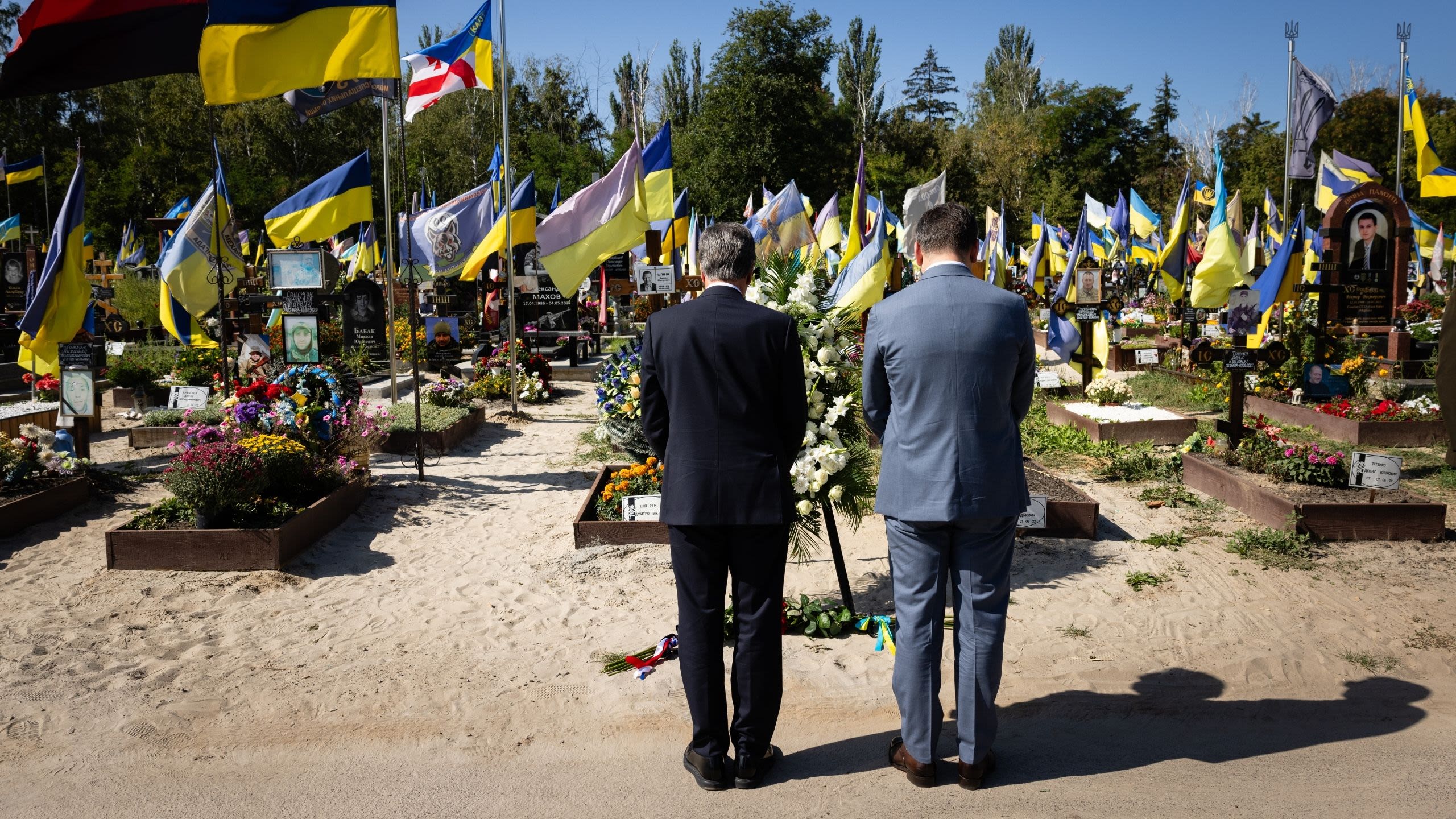 The backs of two men bowing heads in prayer at a cemetery