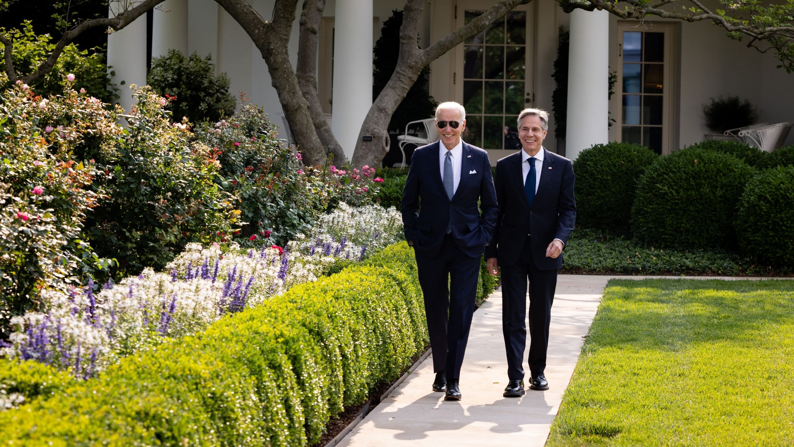 President Biden and Secretary Blinken smiling while walking in the Rose Garden at the White House