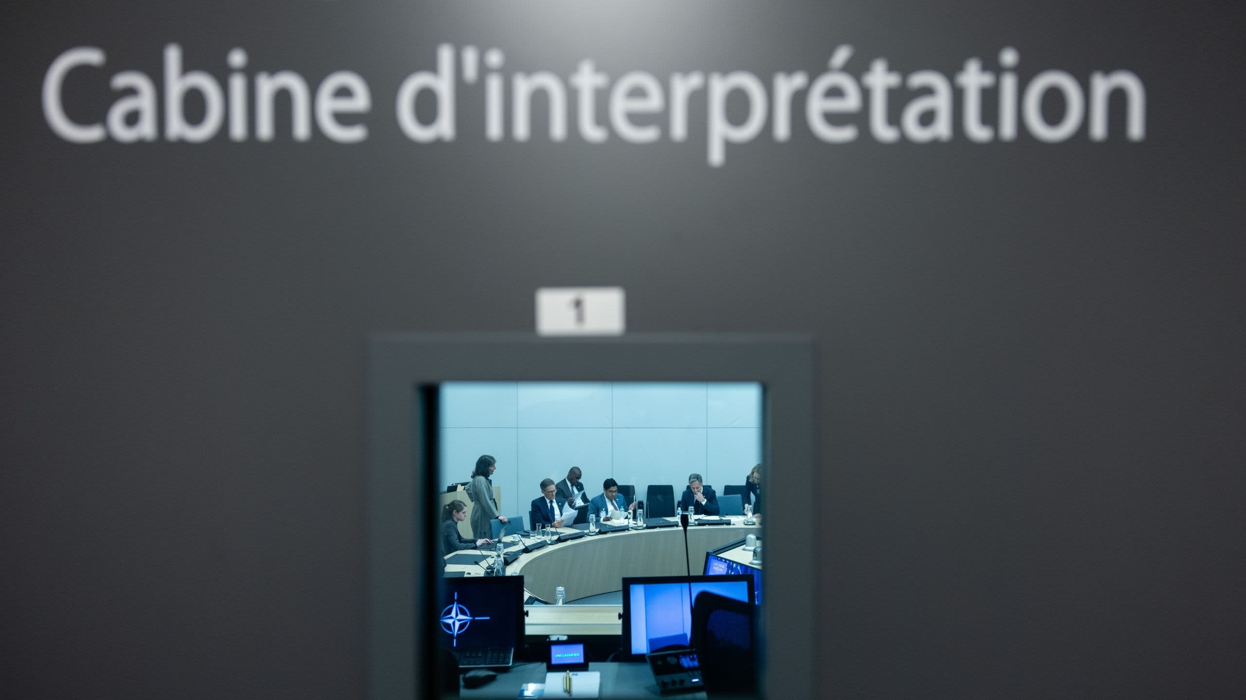 People sitting at a curved table seen through a window on a door that reads “Cabine d’interpretation”