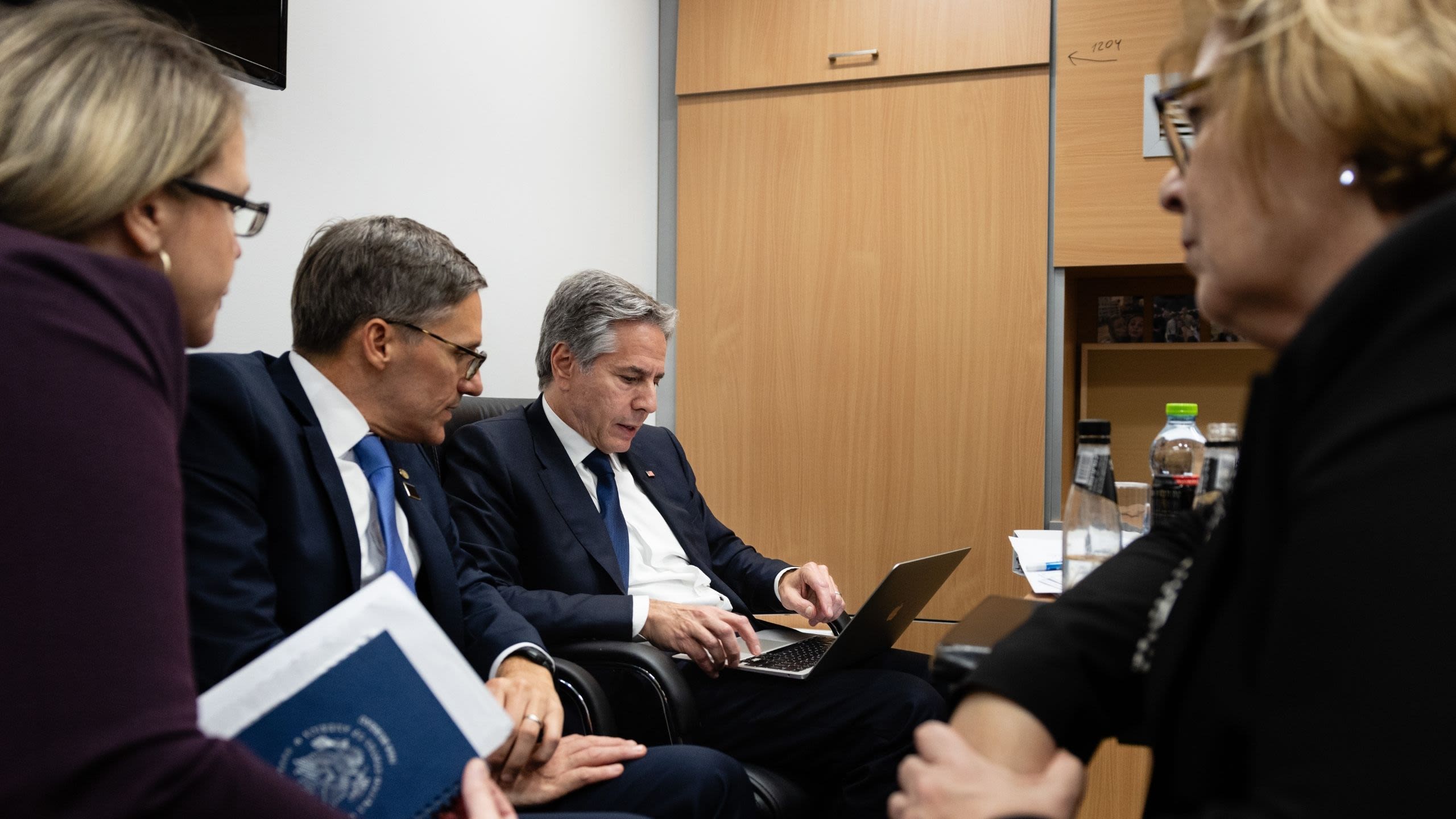 Secretary Blinken looking at a computer while seated with staff 