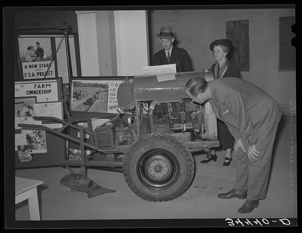 Man examines a small tractor on display at an exhibit (Library of Congress/FSA/Russell Lee)