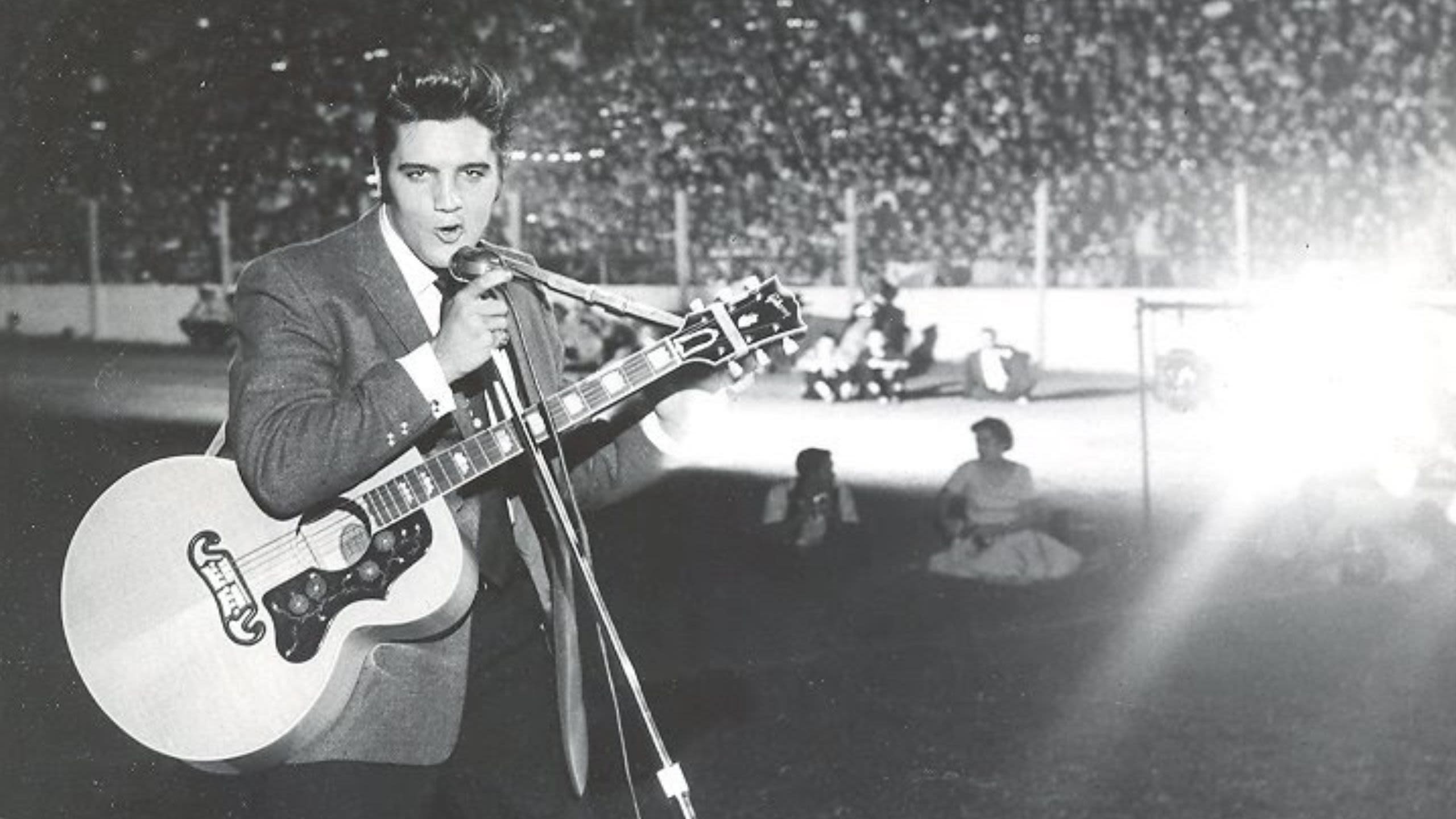 Black-and-white photo of Elvis Presley performing with a guitar before a large stadium crowd  (Courtesy of State Fair of Texas)