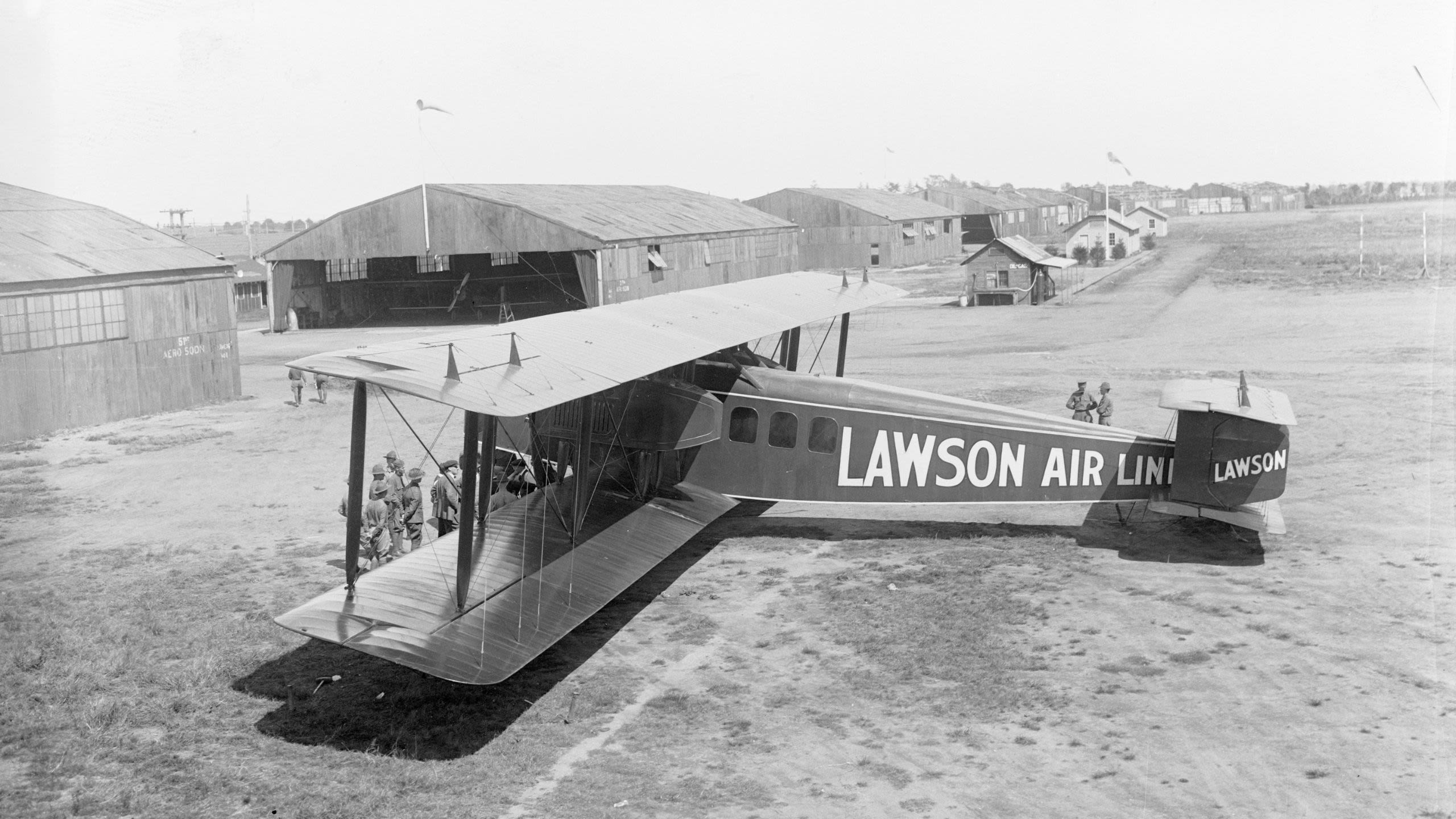 Historic biplane parked near hangars with passengers boarding (© Bettmann/Getty Images)