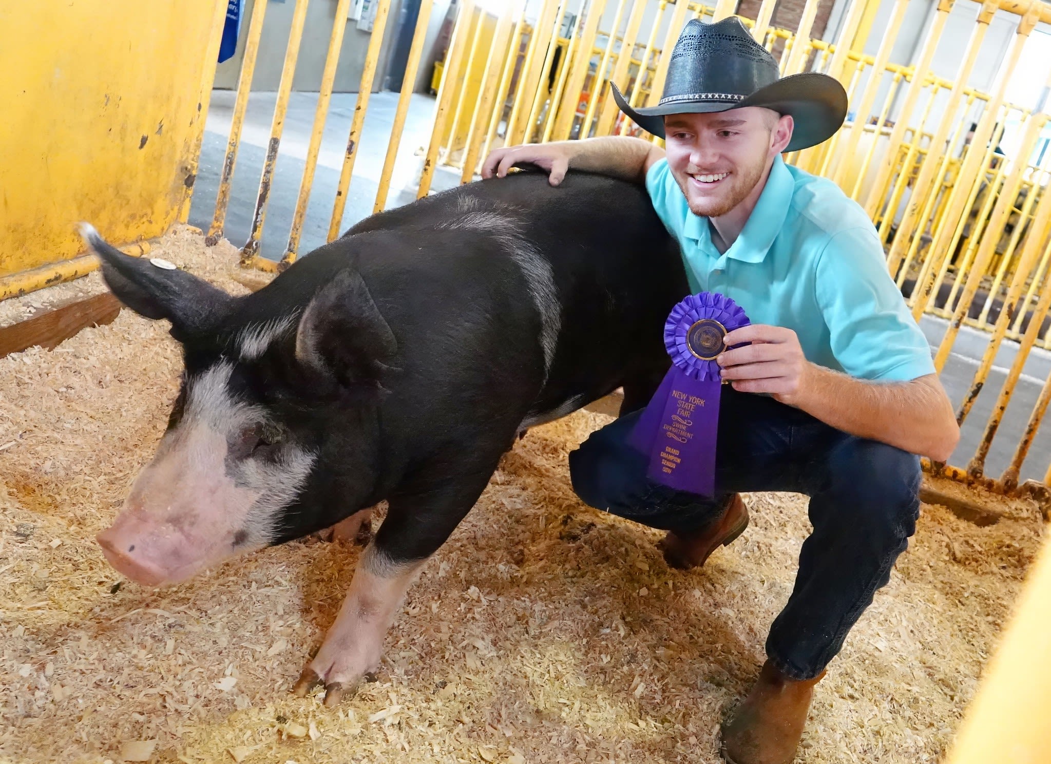 Young man posing with a pig and a champion ribbon (© Michael J. Okoniewski/New York State Fair)