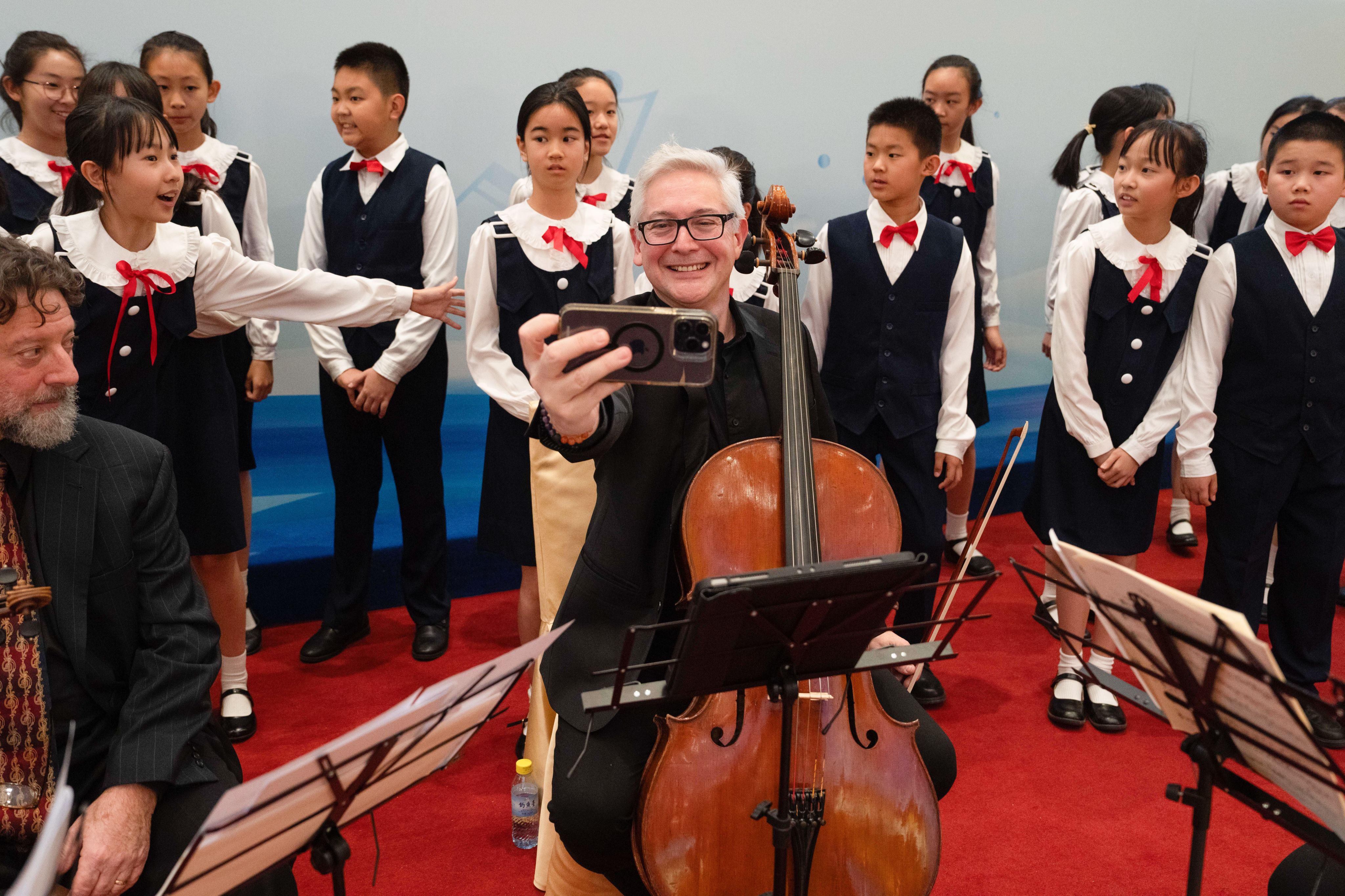 Man with cello taking a selfie in front of a group of children (© Ng Han Guan/AP)