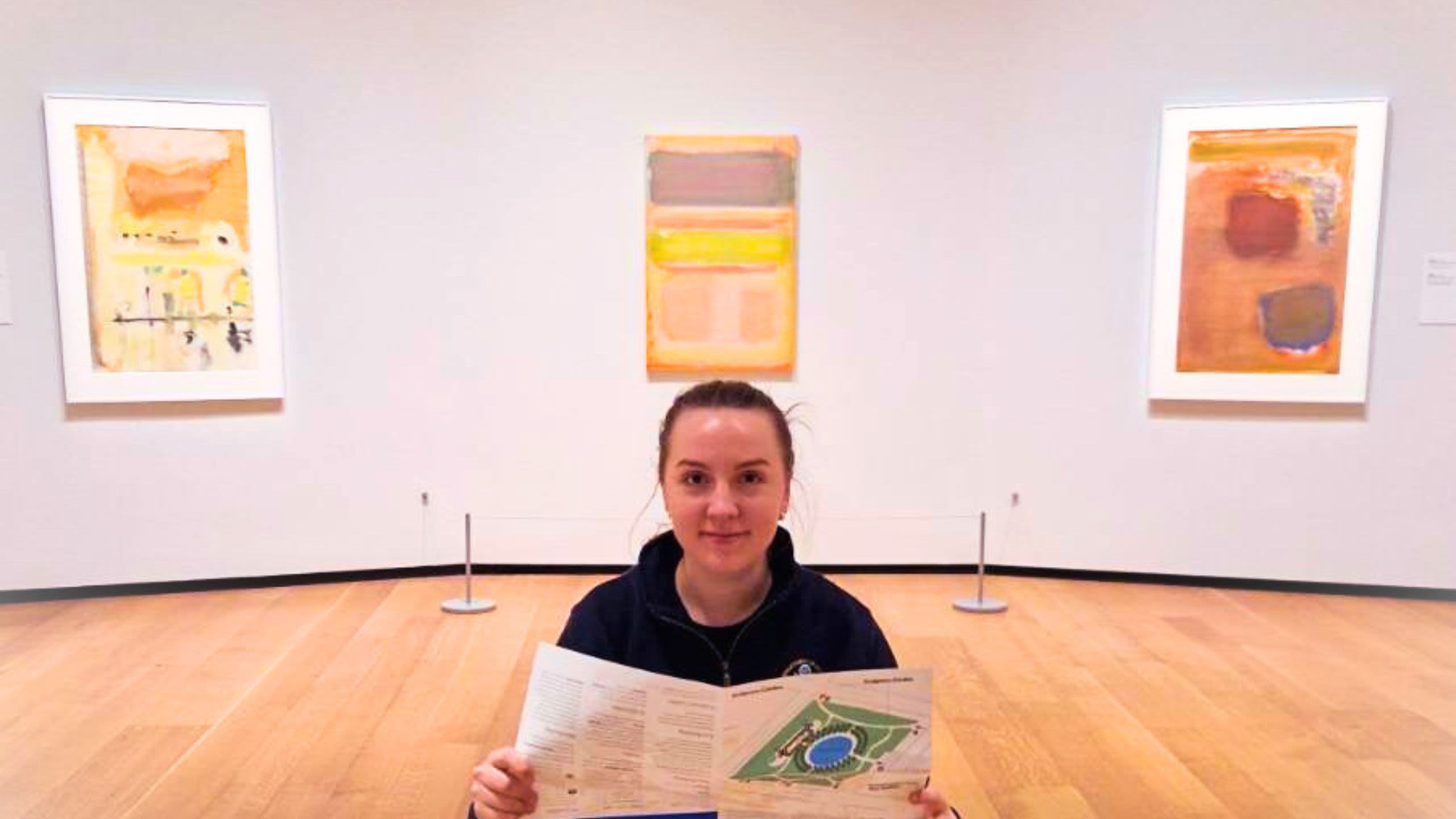 Woman holding a brochure surrounded by artwork (Courtesy of Rūta Beinoriūtė)