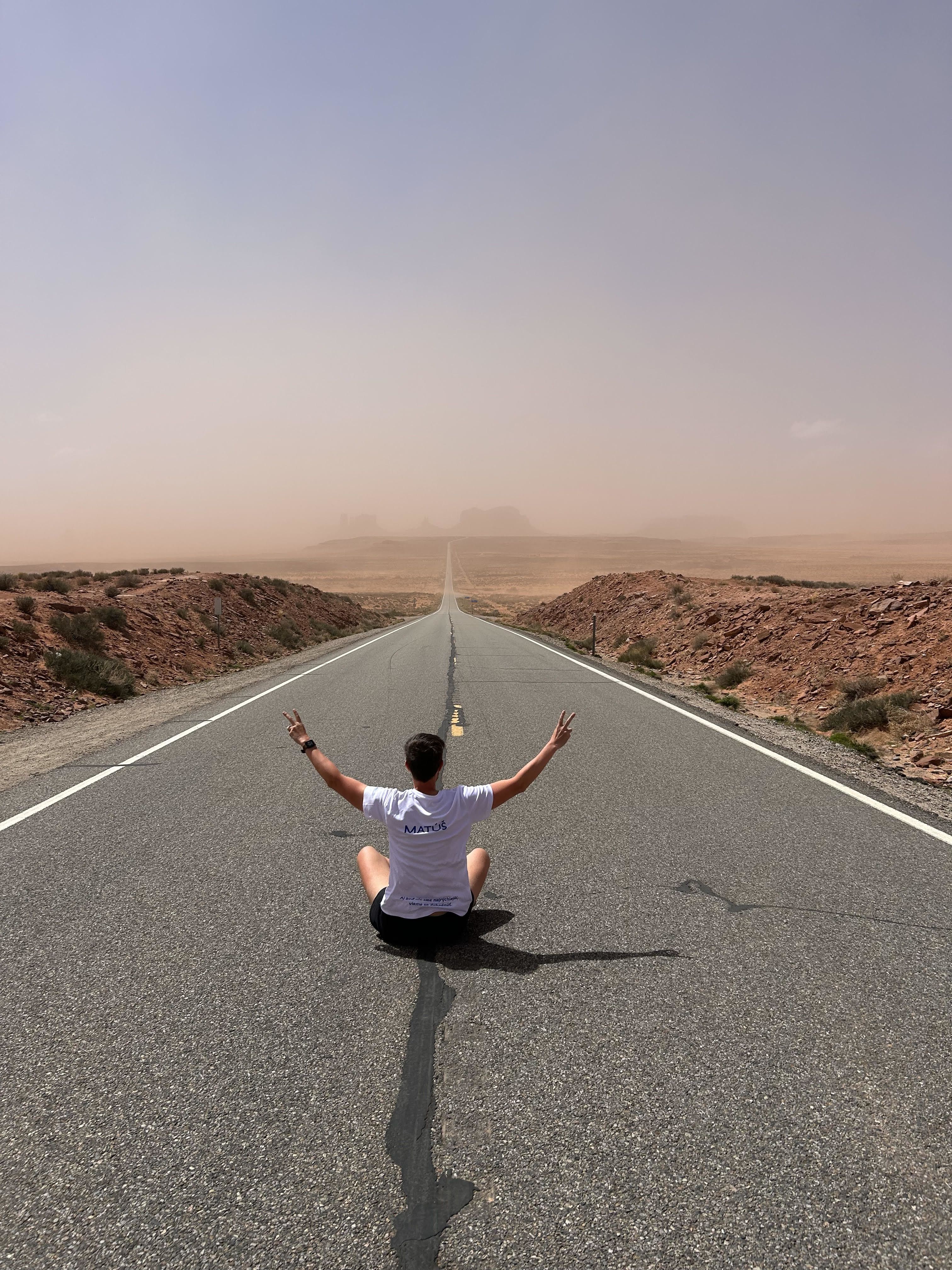Man sitting in the middle of road with arms raised with Monument Valley in the distance Courtesy of Matúš Huťka)