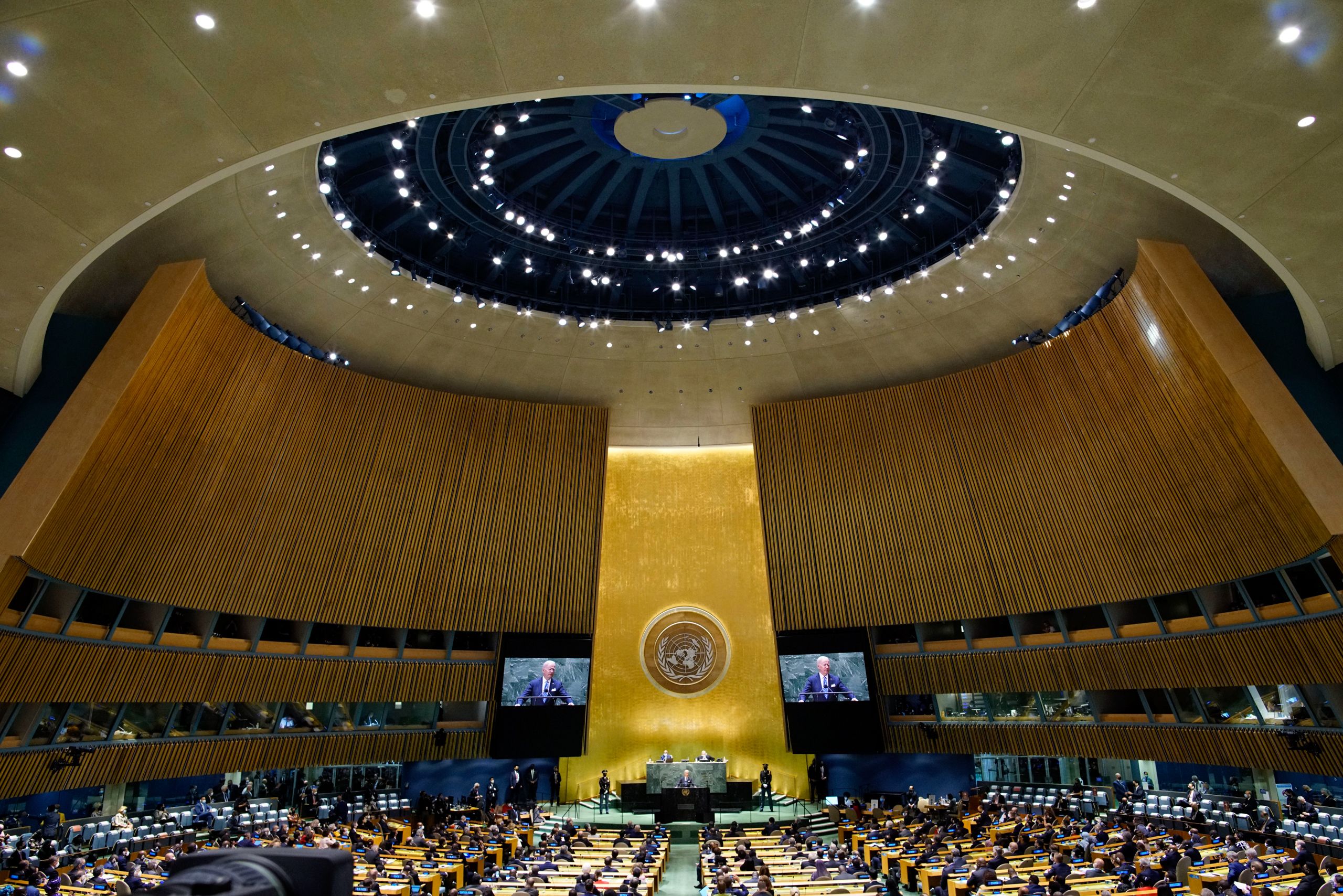 President Biden stands at a podium addressing a large crowd gathered at the United Nations