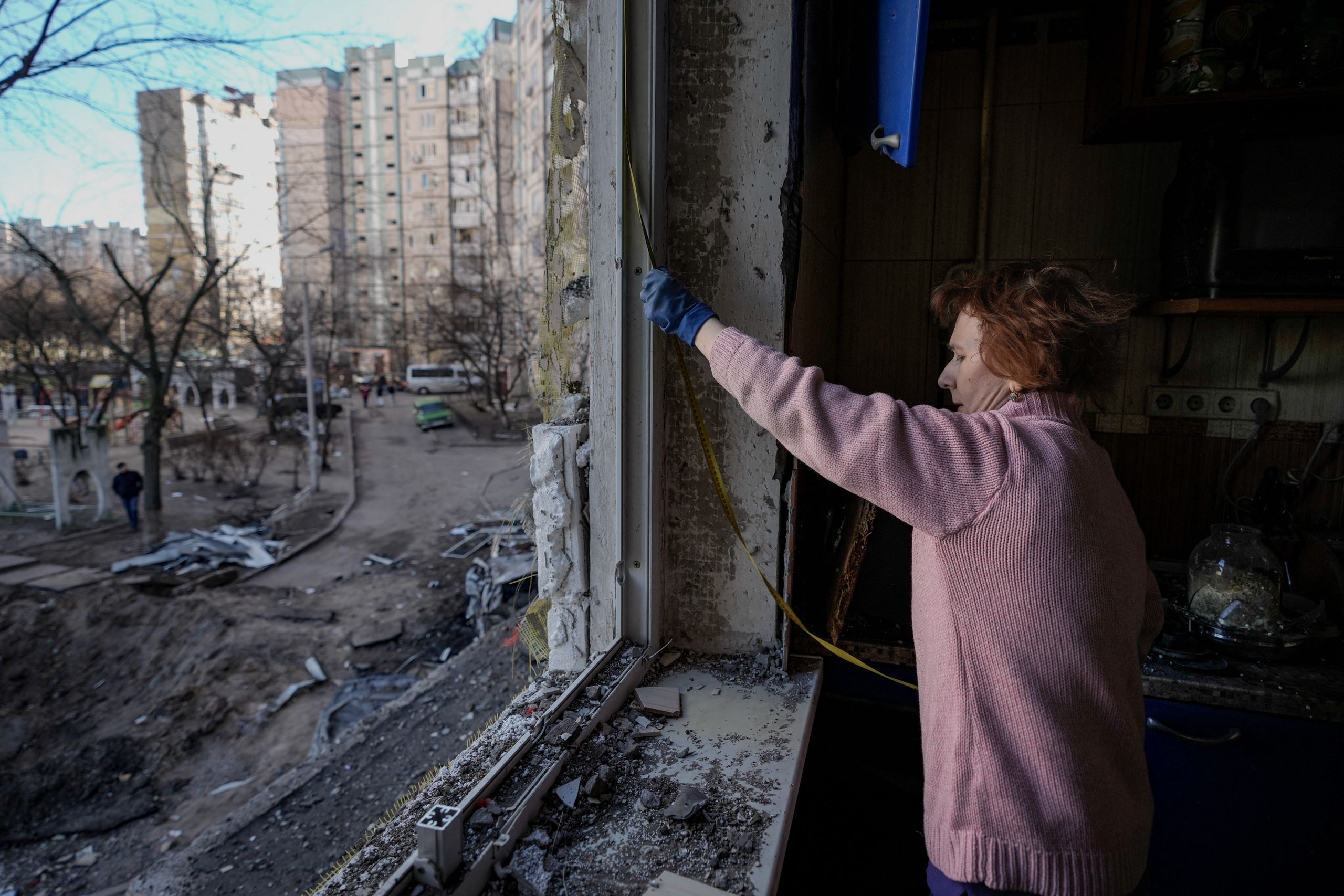 A woman measures a window before covering it with plastic sheets in a building damaged by a bombing the previous day in Kyiv, Ukraine, on March 21, 2022. (© Vadim Ghirda/AP Images)