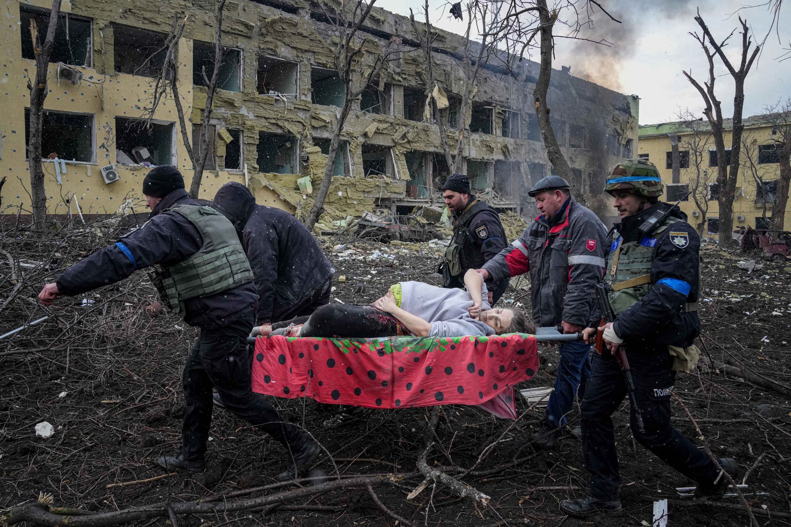 Ukrainian emergency employees and volunteers carry a pregnant woman who suffered a crushed pelvis and detached hip during the shelling of a maternity hospital in Mariupol, Ukraine, on March 9, 2022. The woman and her baby later died. (© Evgeniy Maloletka/AP Images)