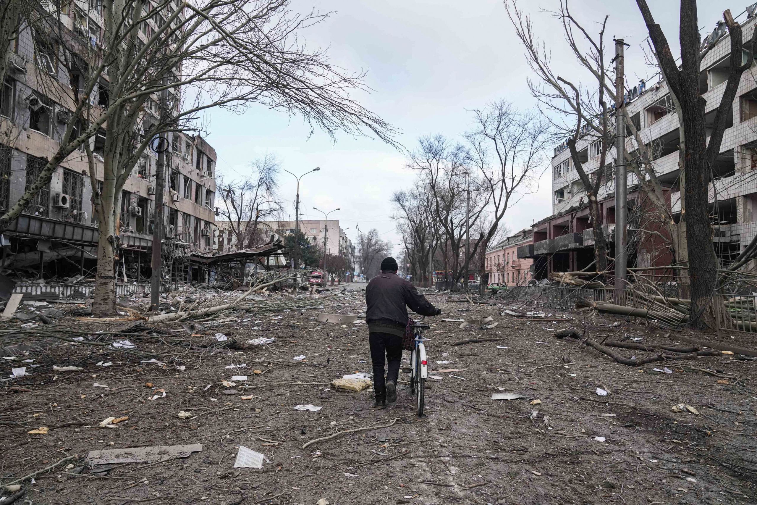 A man walks with a bicycle in a street damaged by shelling in Mariupol, Ukraine, on March 10, 2022. (© Evgeniy Maloletka/AP Images)
