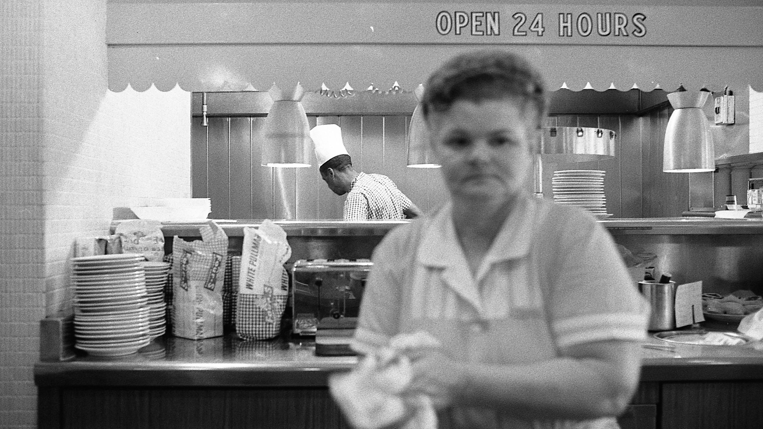 Diner counter with “OPEN 24 HOURS” sign and cook and server (© Robert Abbott Sengstacke/Getty Images)