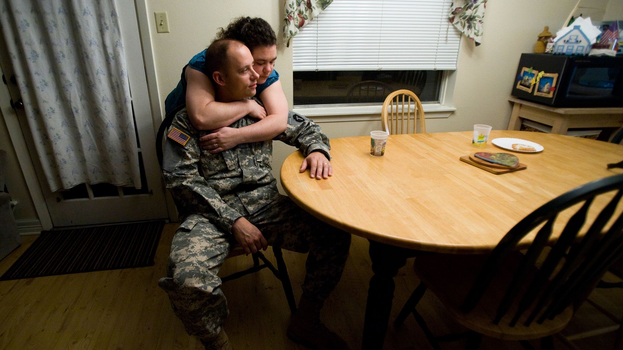 Man in uniform sitting at kitchen table as woman hugs him from behind (© Mayra Beltran/Houston Chronicle/Getty Images) 