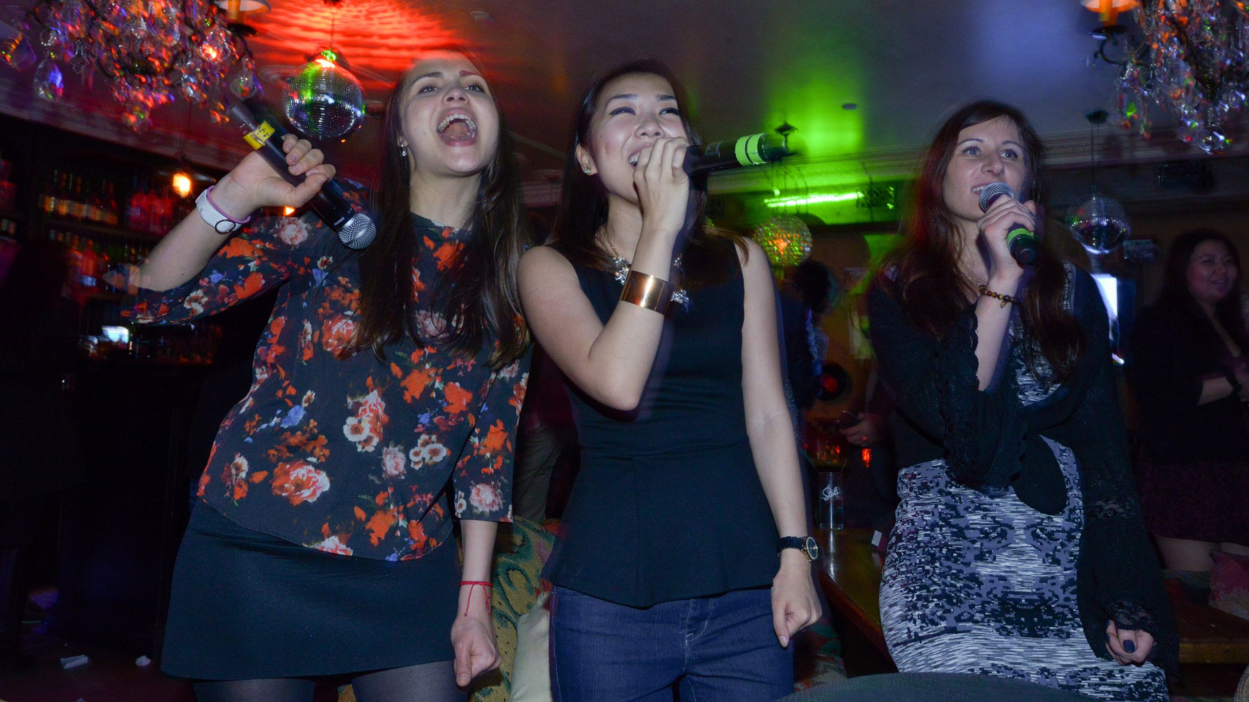 Women holding microphones and singing karaoke under colorful lights (© Molly Riley/Washington Post/Getty Images)
