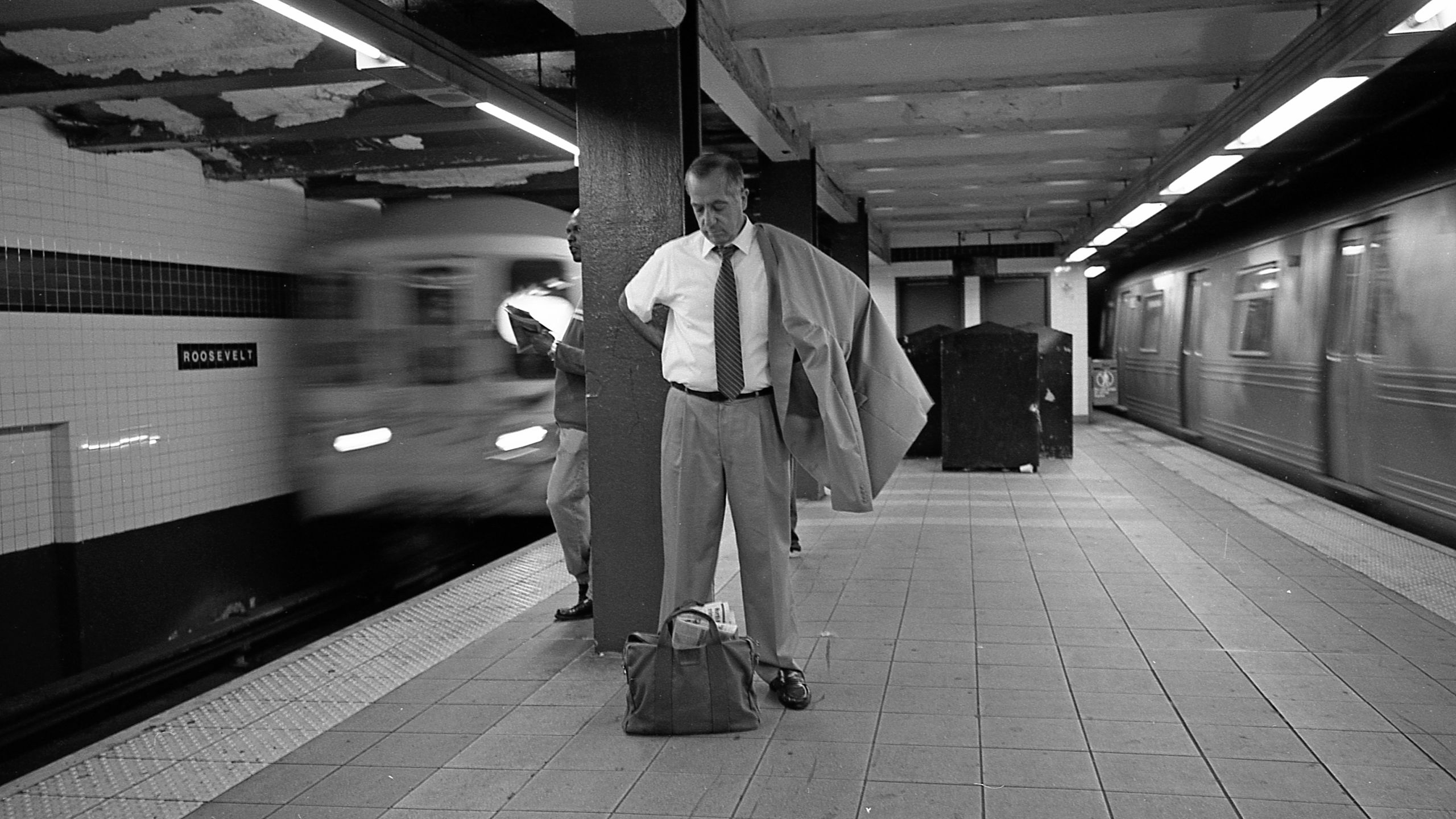 Man standing on subway platform between two trains, duffel at his feet (© Walter Leporati/Getty Images)